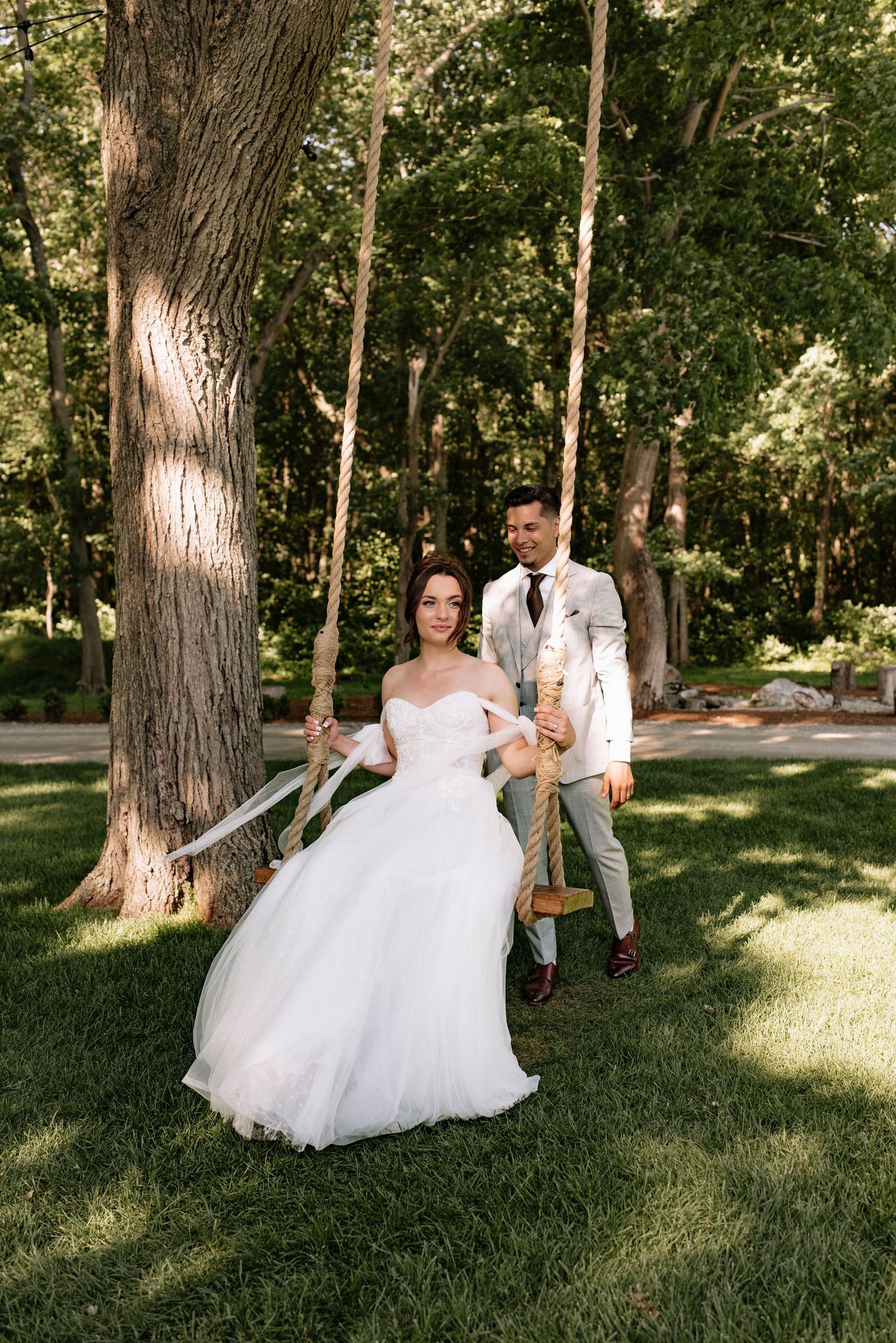 A bride on a swing being pushed by her groom in an elegant garden setting.