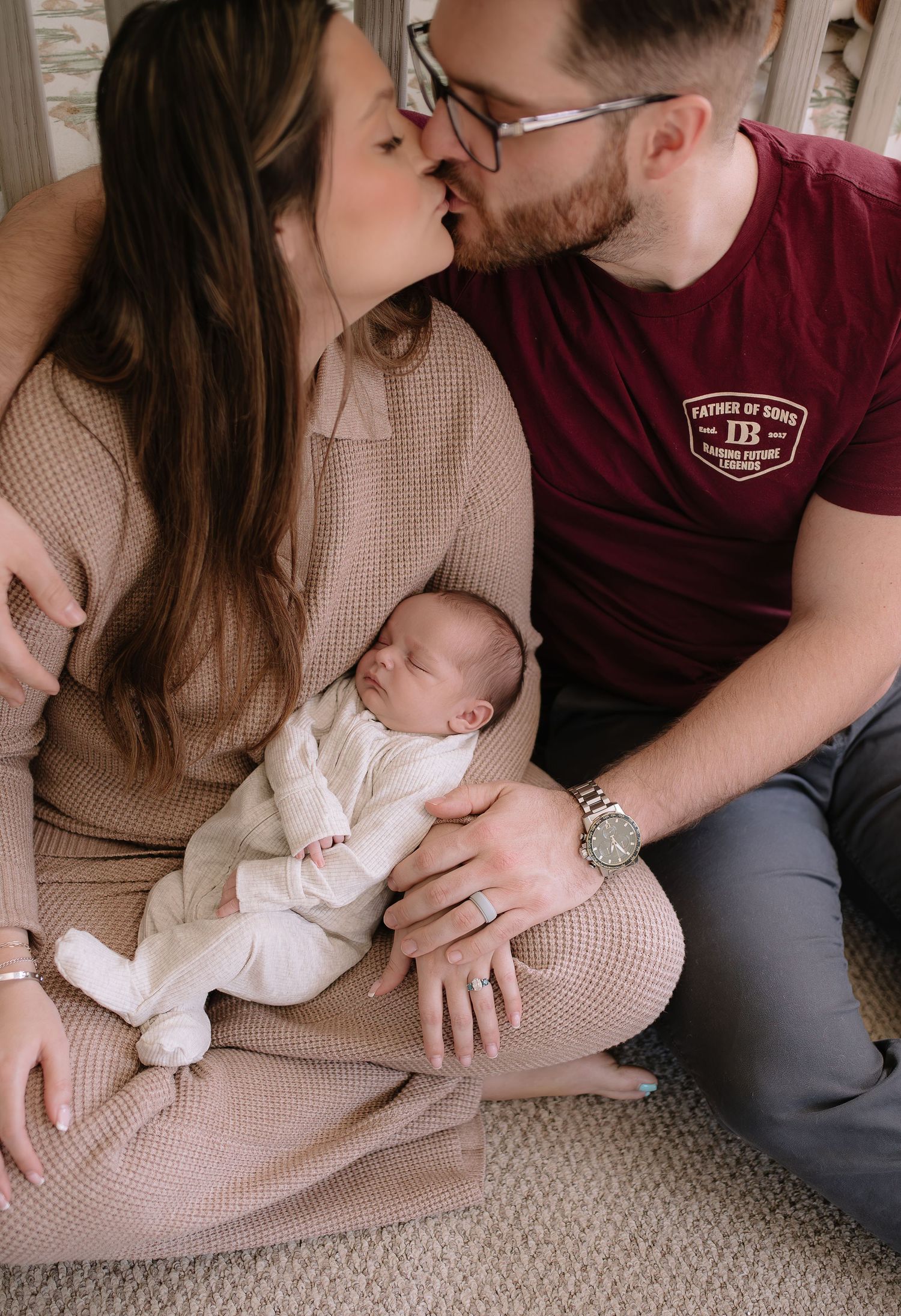 An intimate family moment as parents share a kiss while holding their sleeping newborn baby.