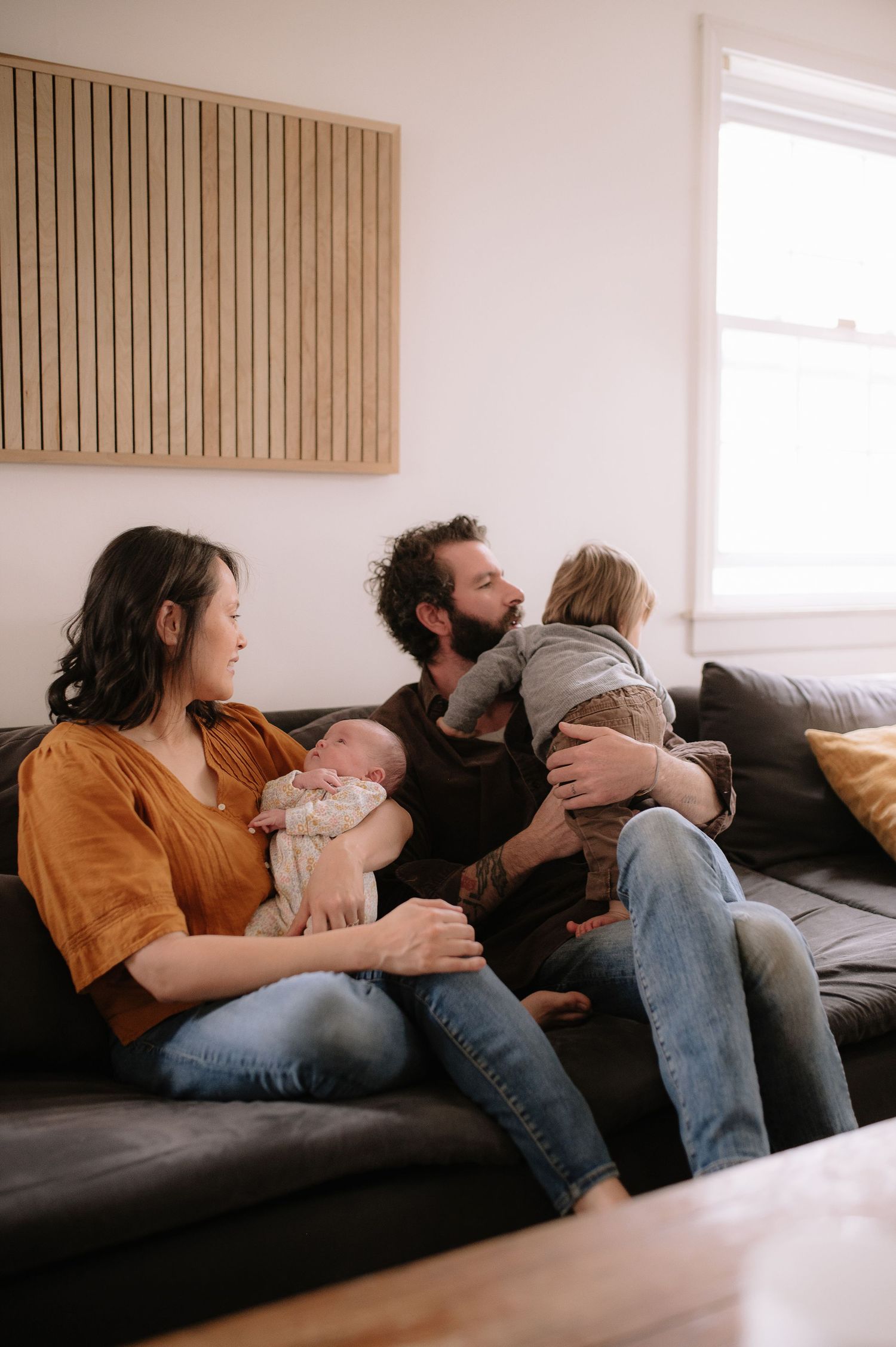 Family relaxing together on a gray couch with their children in a minimalist living room.