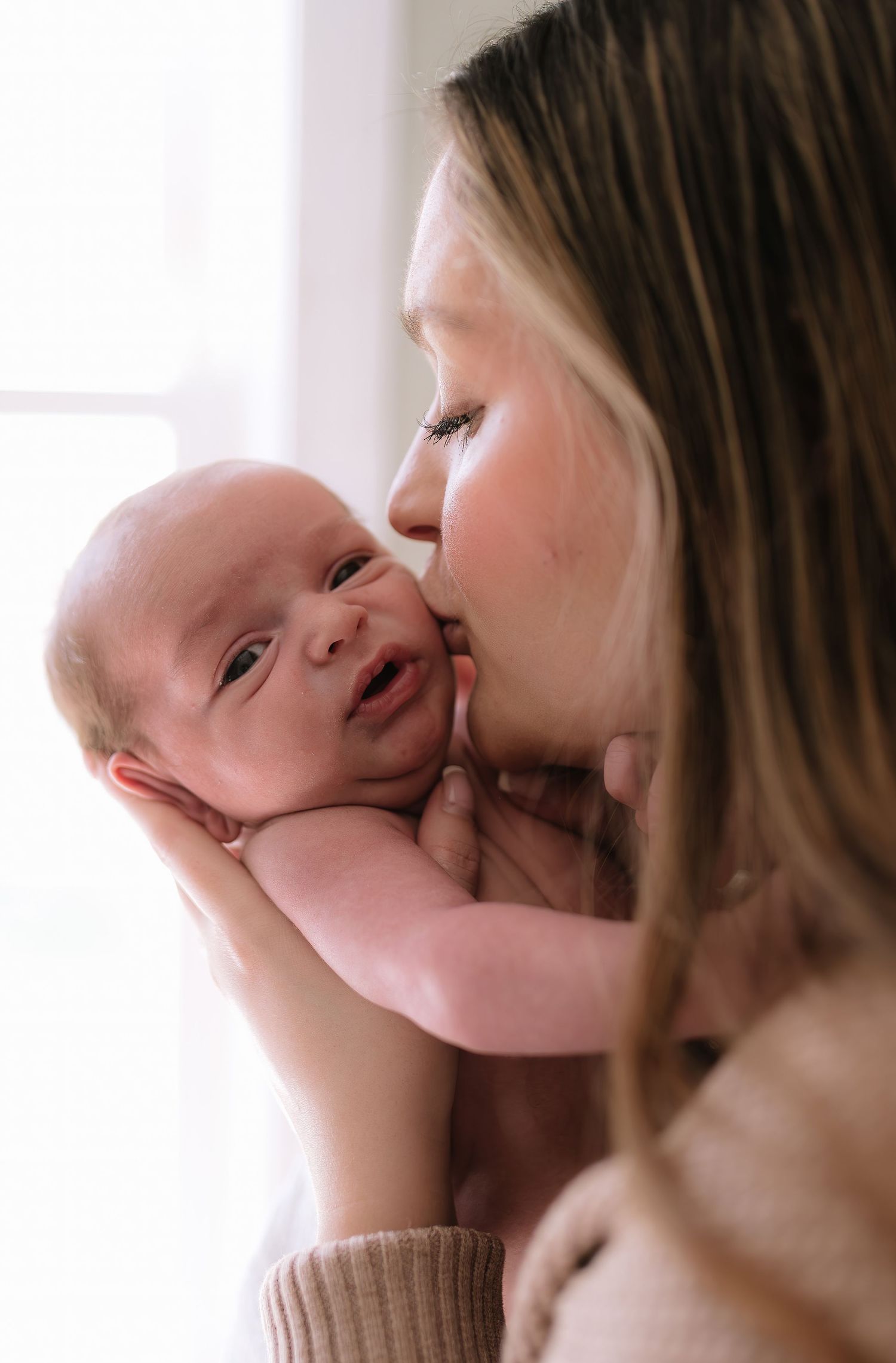 A tender moment between parent and infant in natural window light.