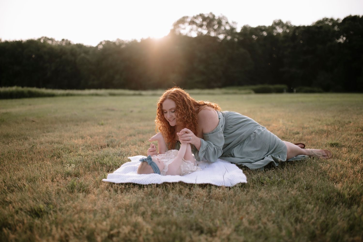 Someone in a denim dress lies reading on a blanket in a grassy field at sunset.