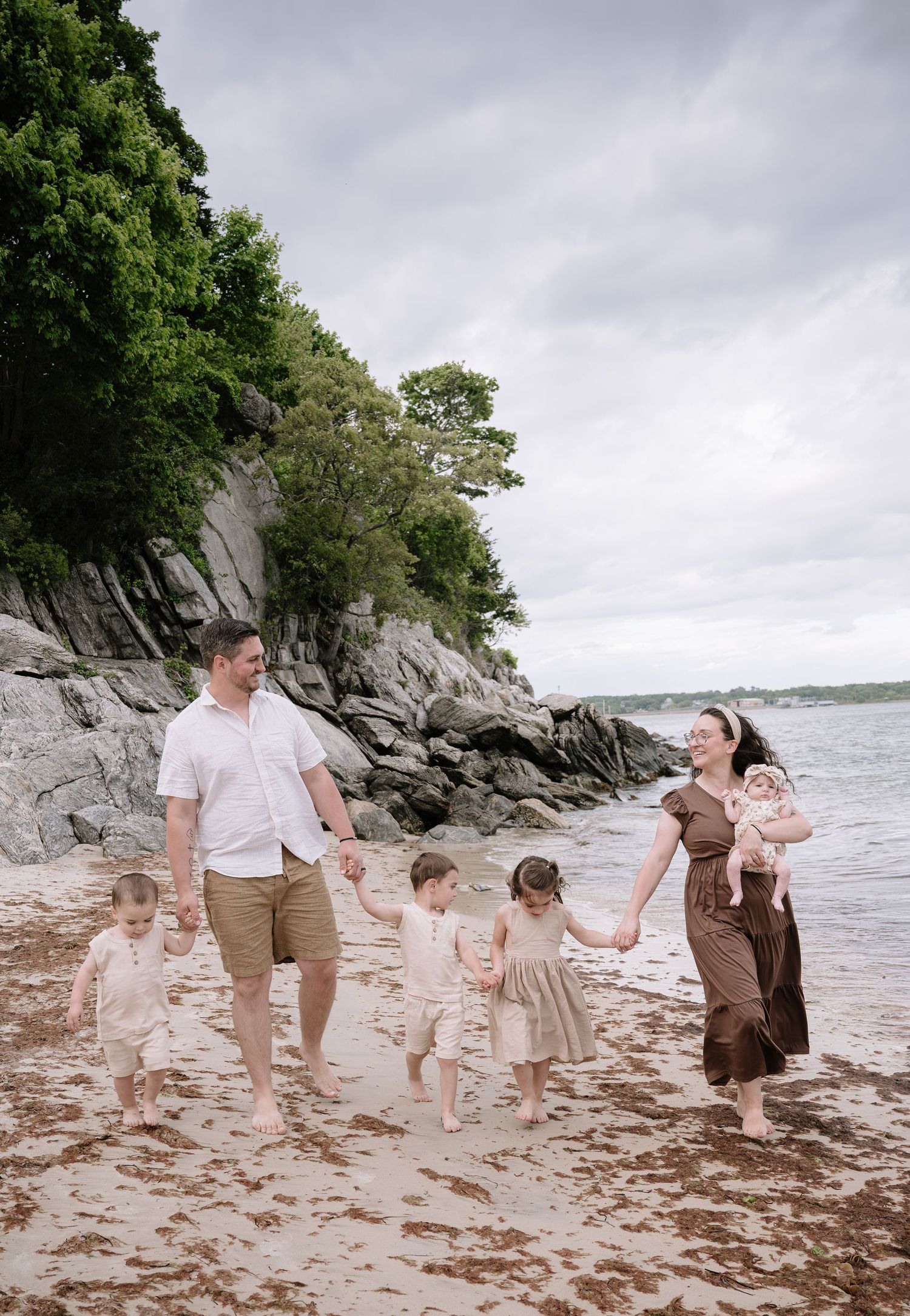 A family in coordinated outfits enjoys a summer day on a rocky beach with dramatic coastal cliffs in the background.