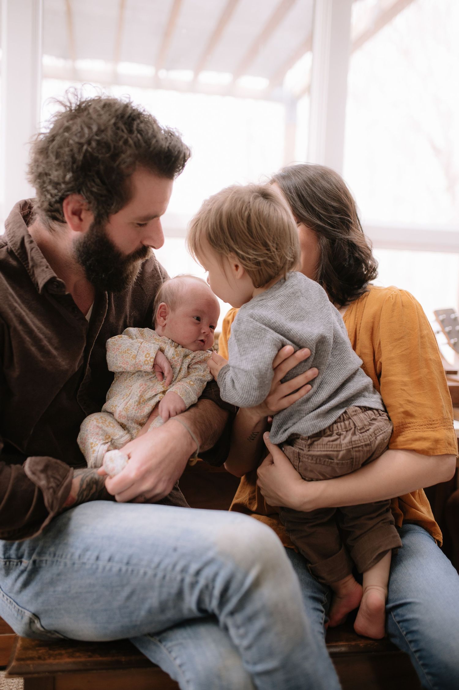 Parents sitting close together with their baby and toddler in a tender family moment.
