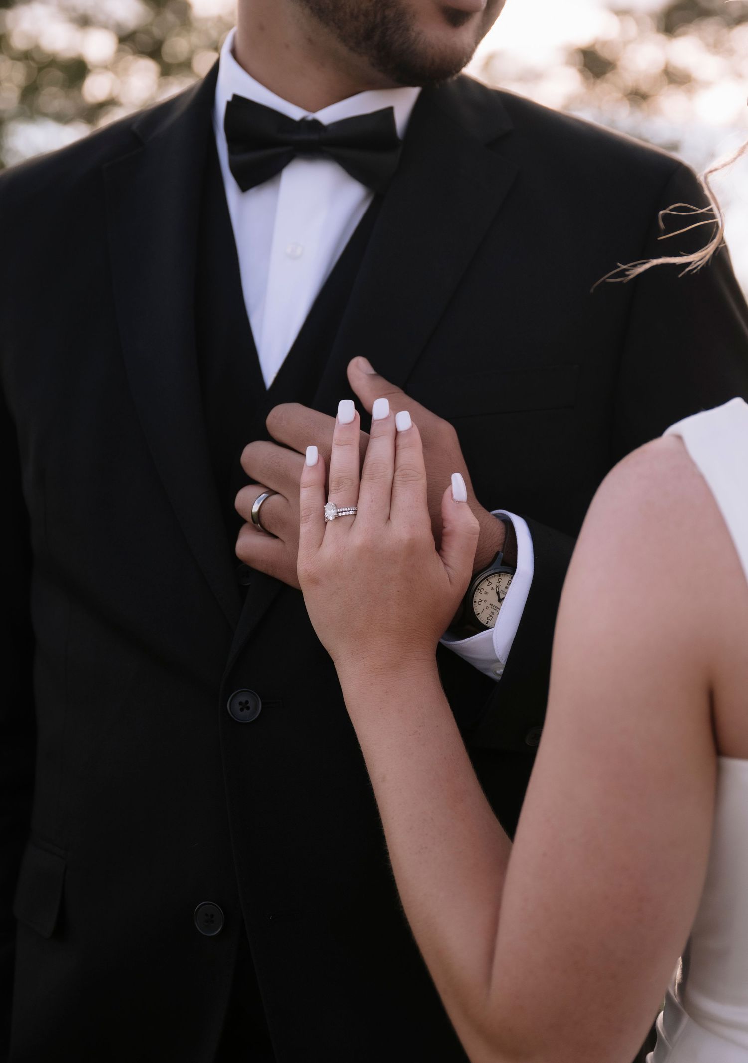 Close-up details of wedding rings and hands against formal black and white attire.