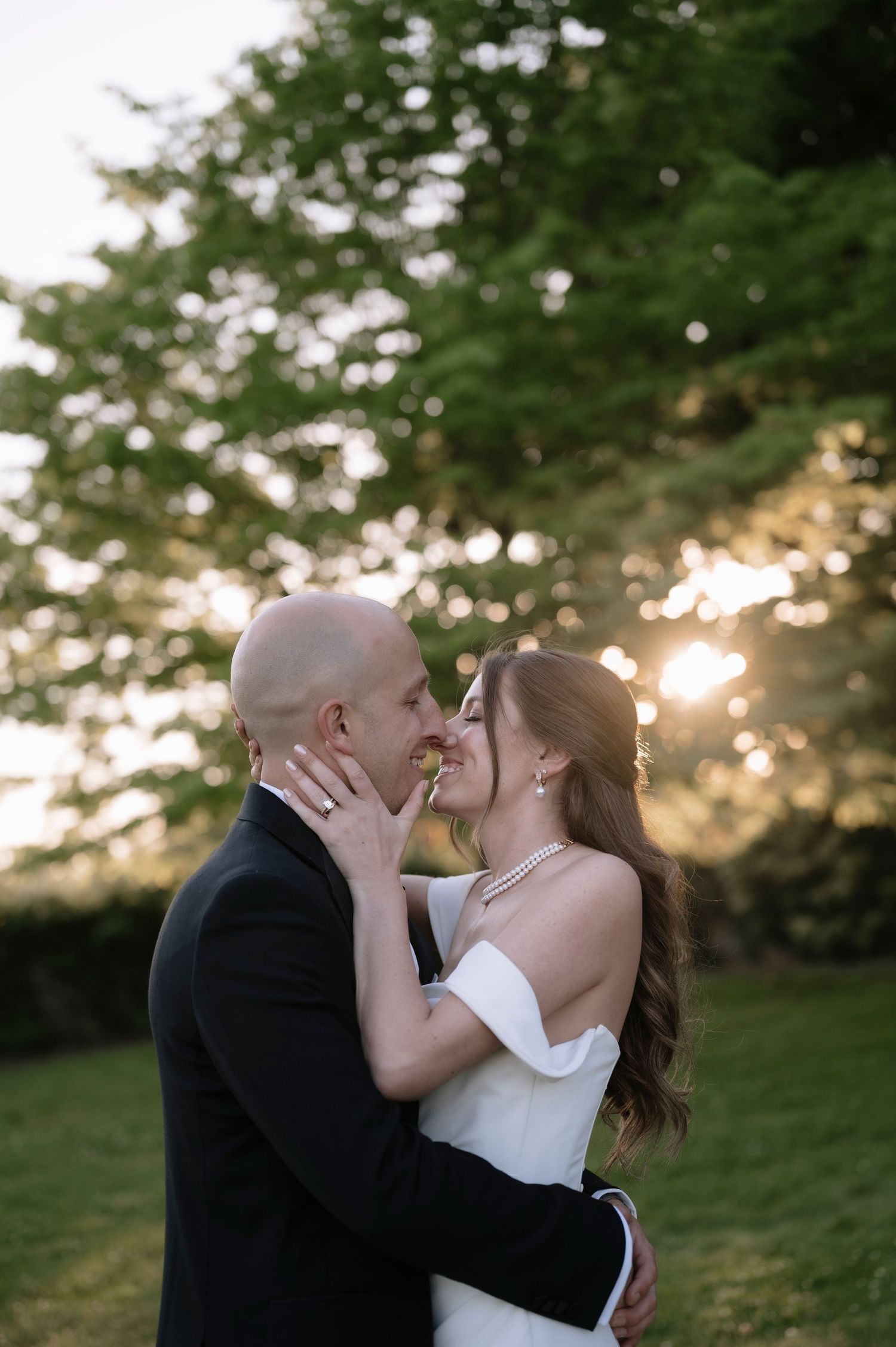 A couple shares a romantic sunset kiss on their wedding day in a green outdoor setting.