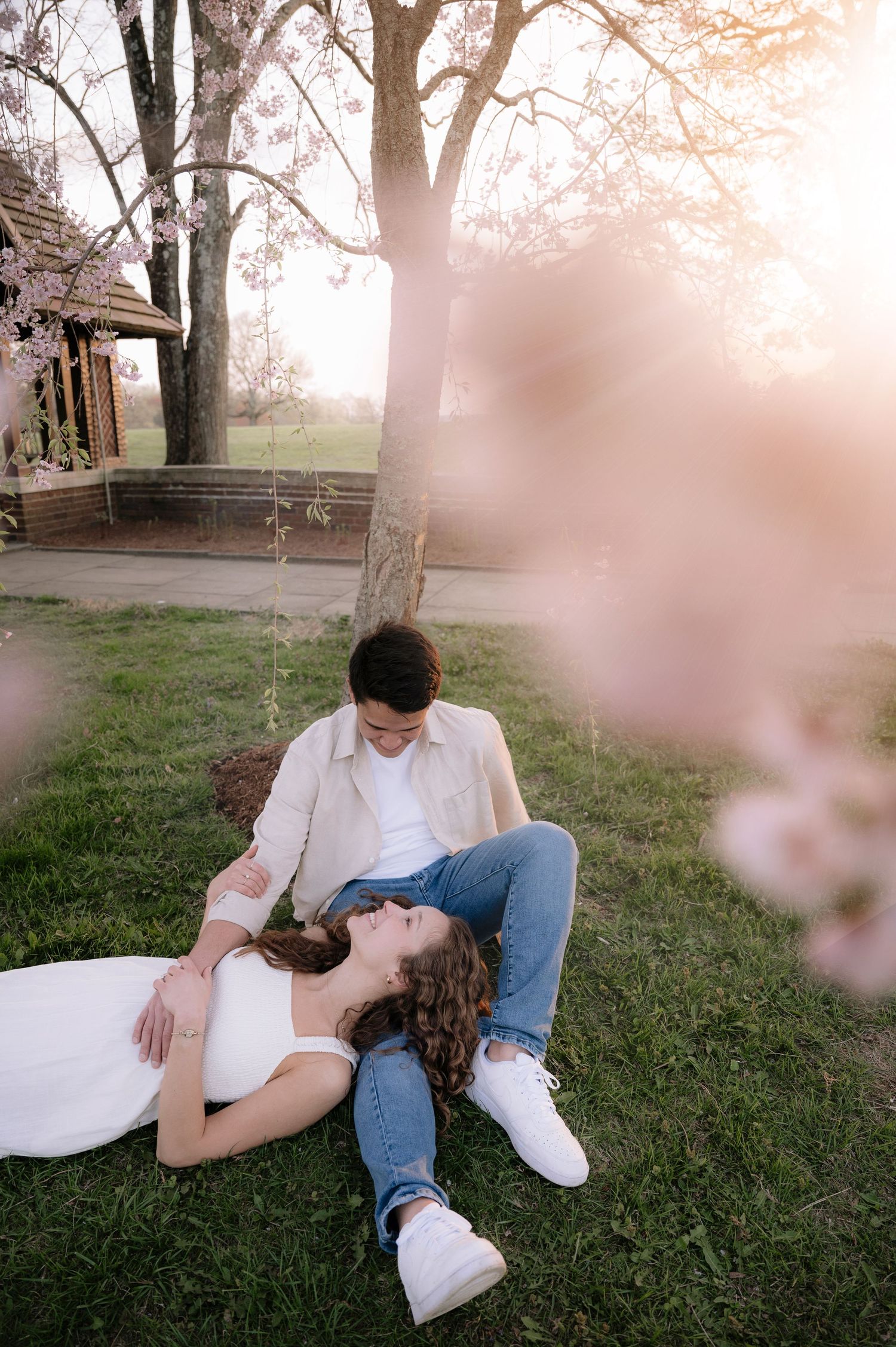 Intimate moment on lawn beneath blooming spring trees near rustic building.
