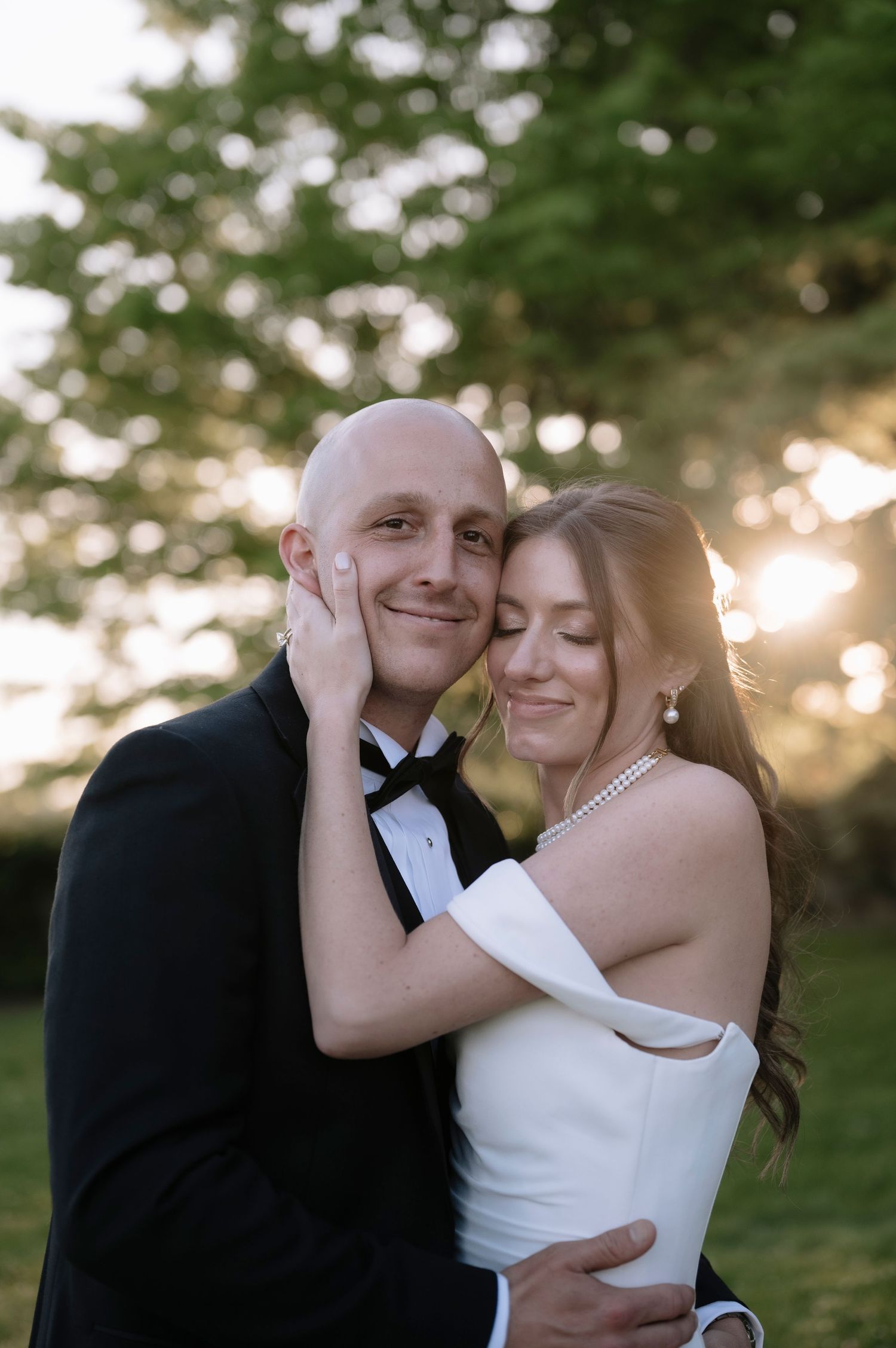 A romantic newlywed couple poses together in a sunset-lit garden setting wearing formal wedding attire.