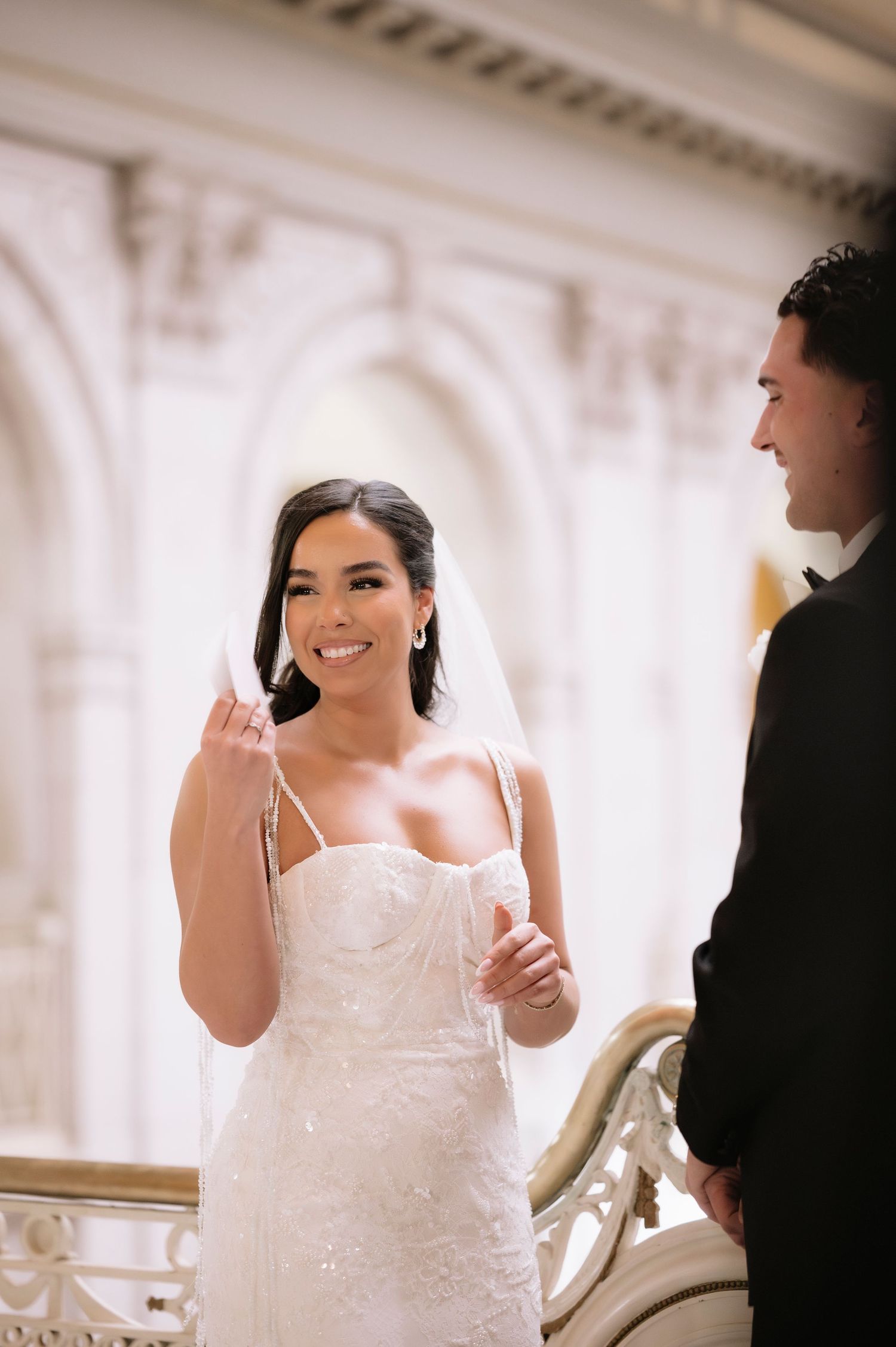 Radiant bride in beaded gown smiles joyfully at groom during ceremony.