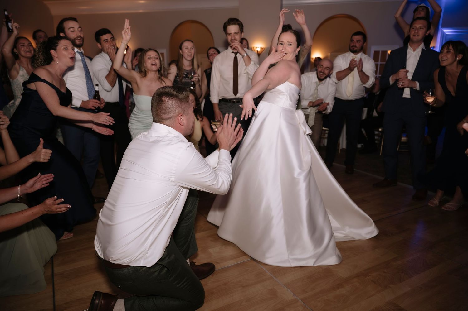Bride and groom dancing joyfully at wedding reception surrounded by cheering guests on the dance floor.