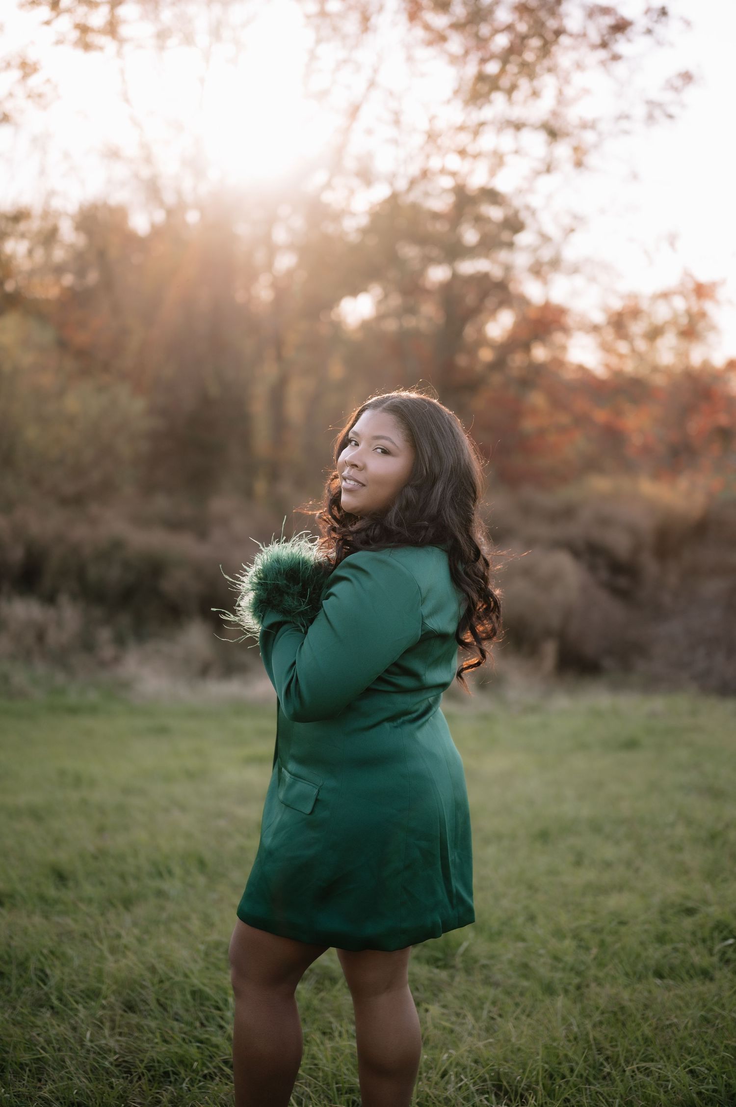 A child in a green winter coat twirls playfully in a grassy field during golden hour sunset.