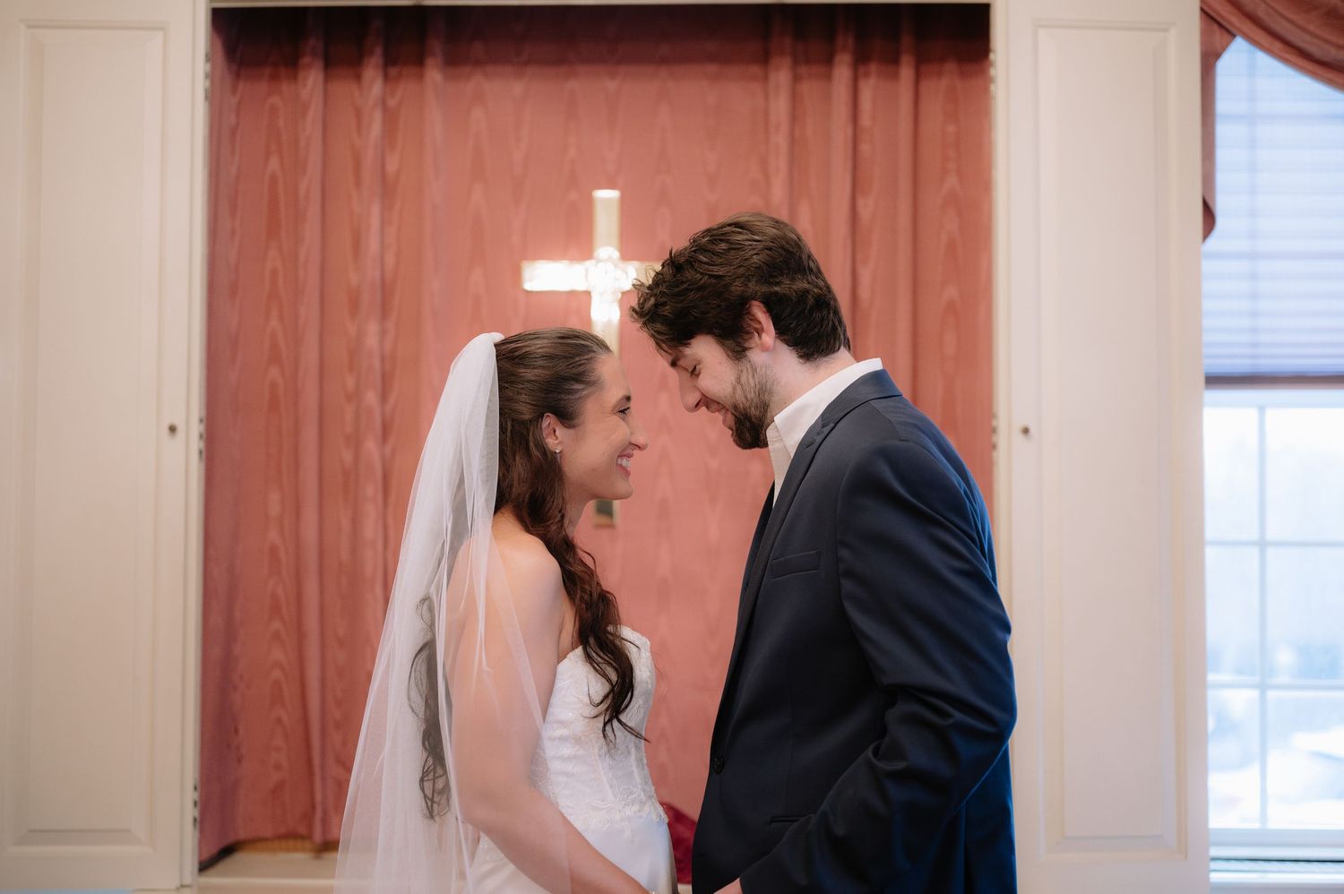 Intimate wedding moment in front of a rustic red door with white cross detail.