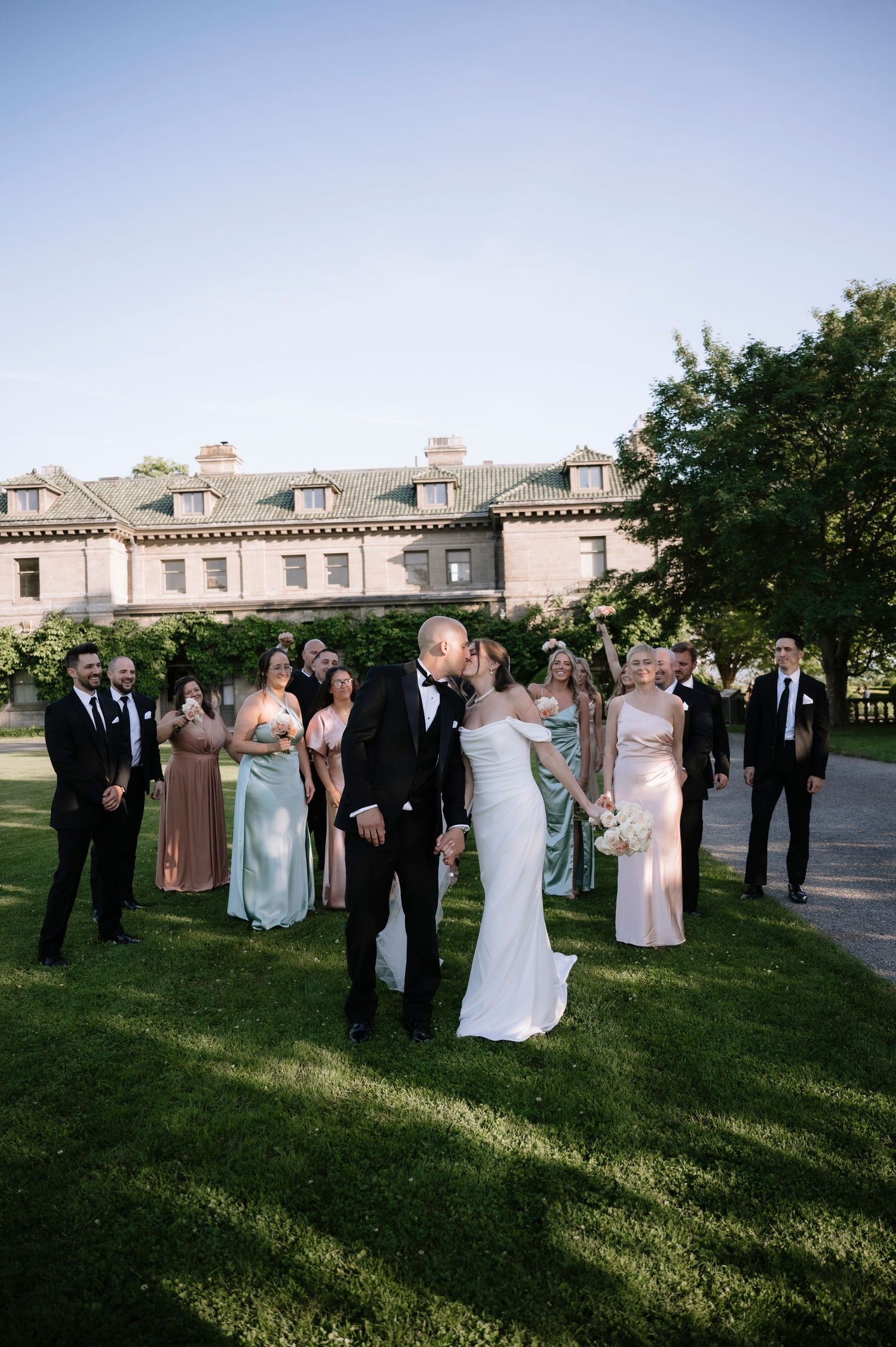 Wedding party gathered outdoors at sunset casting long shadows on grass during outdoor ceremony reception.