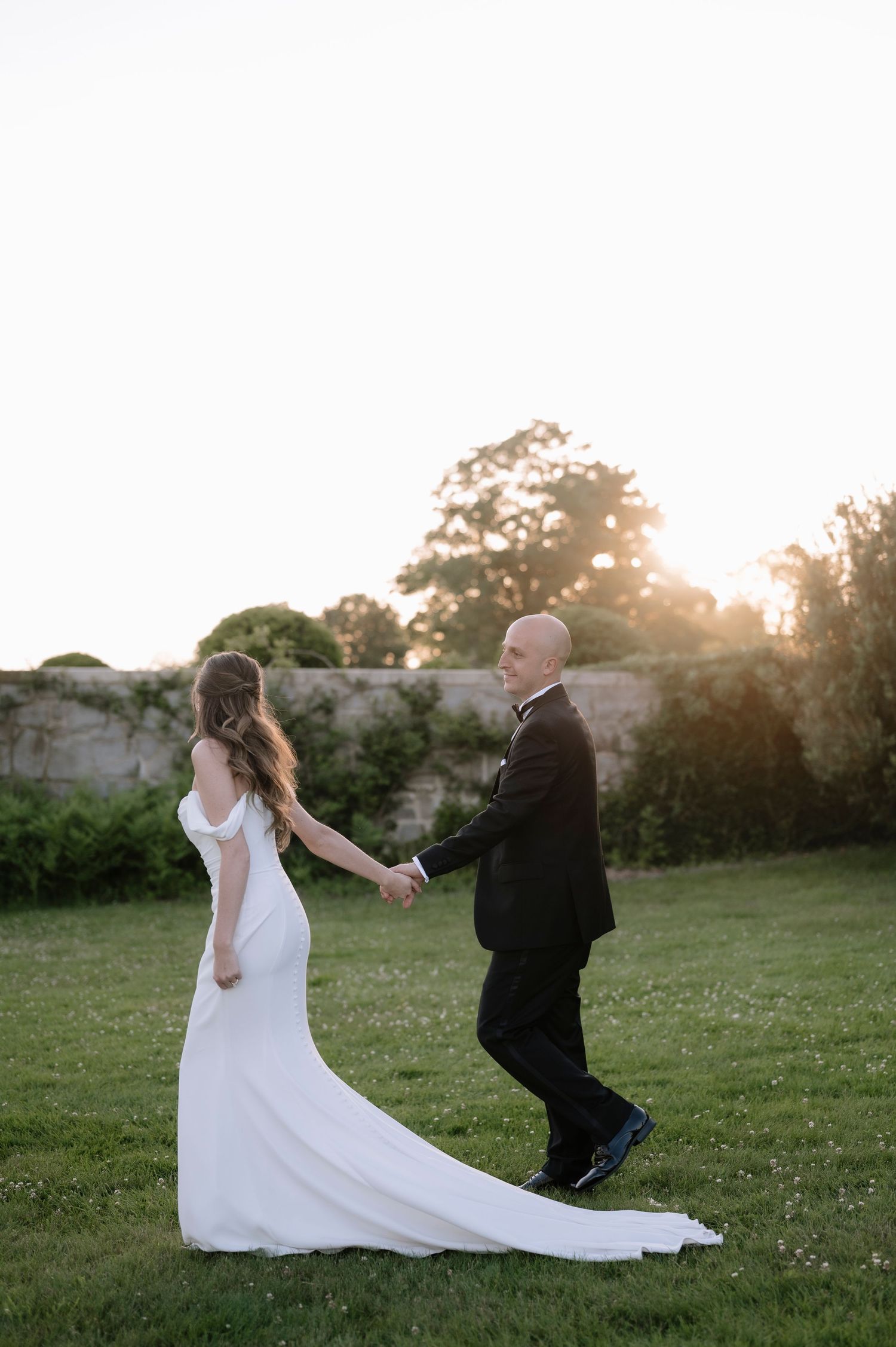 A romantic moment captured at sunset shows a couple dancing and twirling in a grassy field during their wedding.