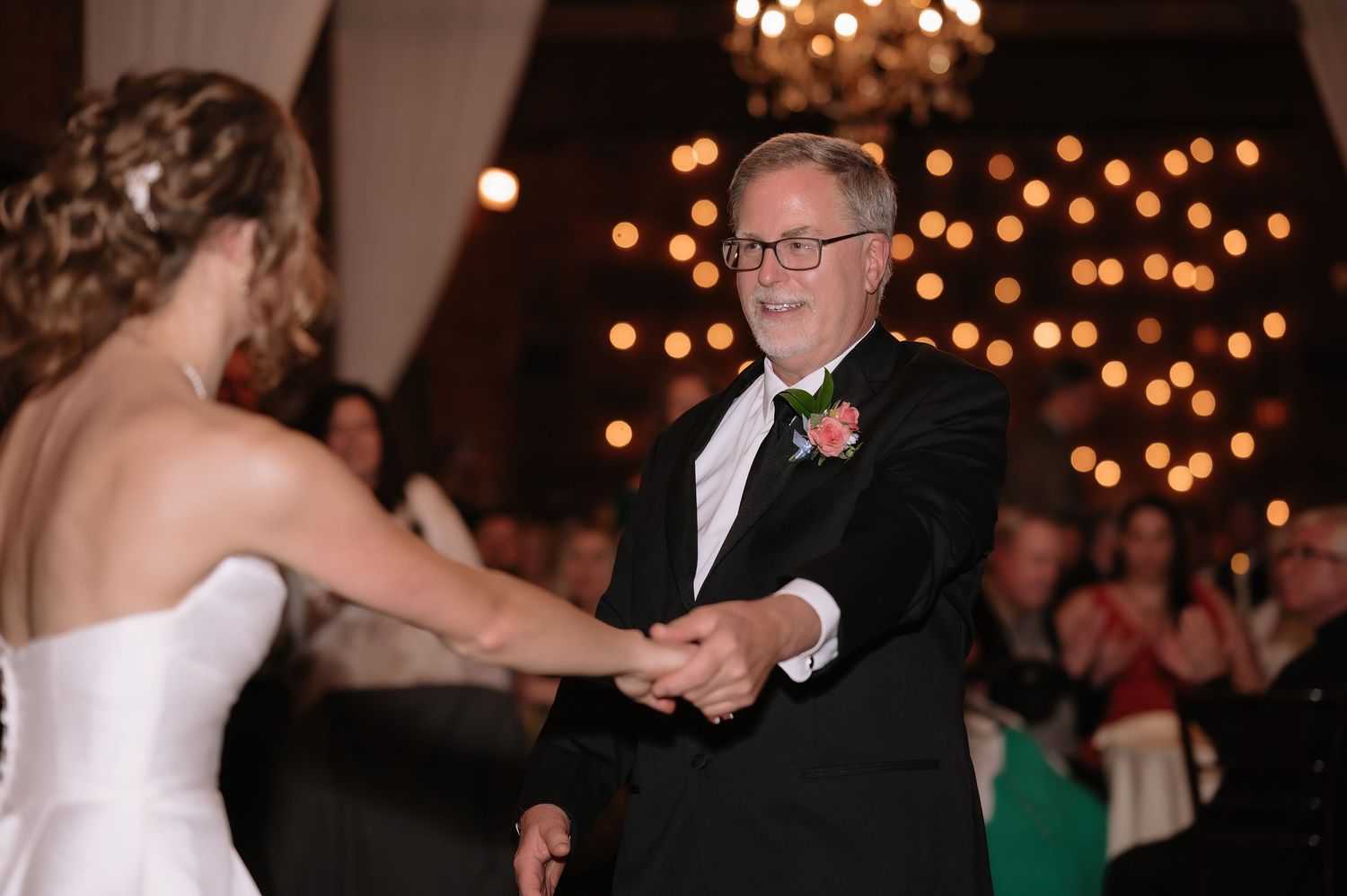 Father and daughter share a joyful first dance at an elegant wedding reception with warm bokeh lights in the background.