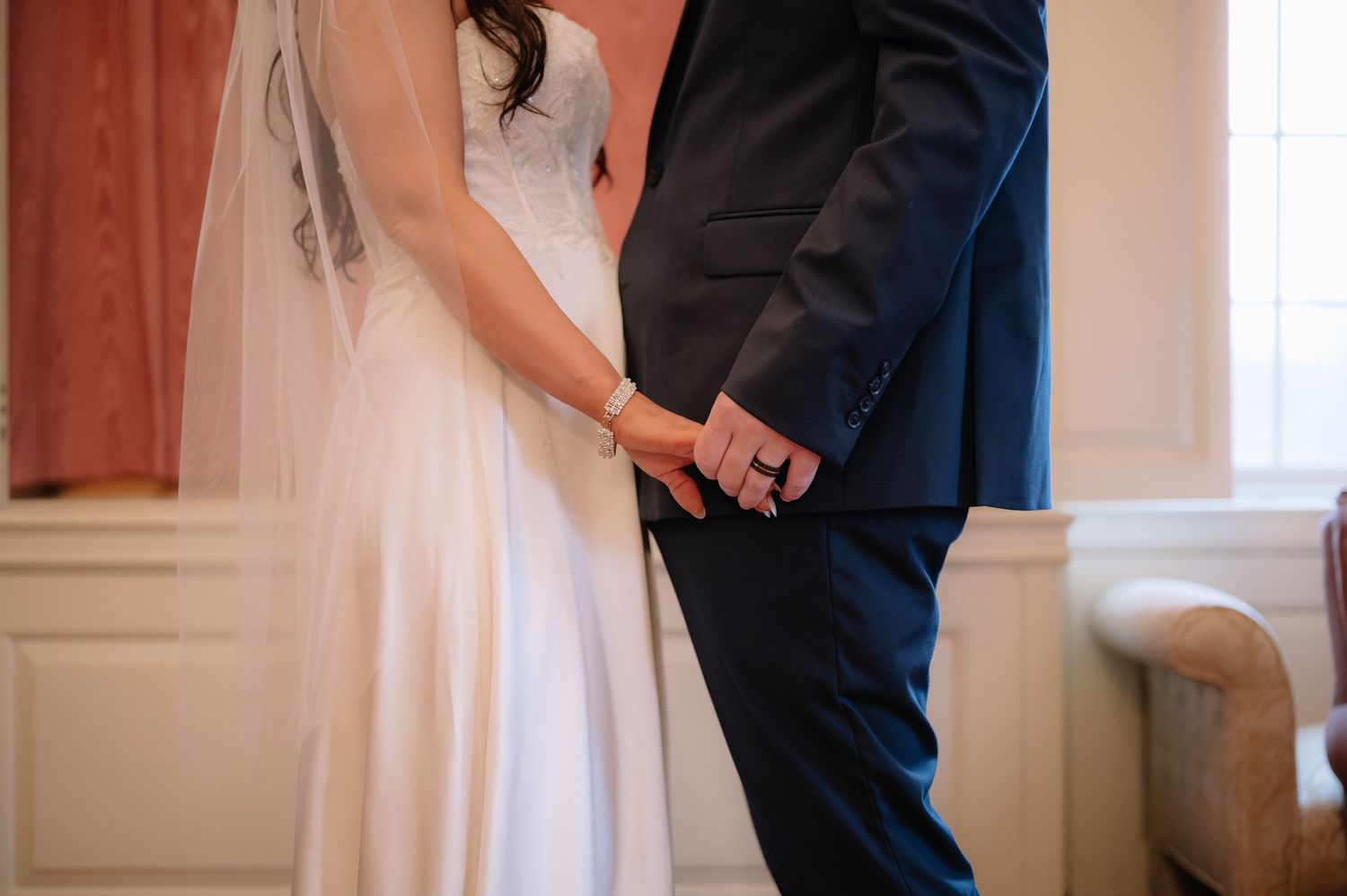Close up of couple holding hands during wedding ceremony in an indoor setting.