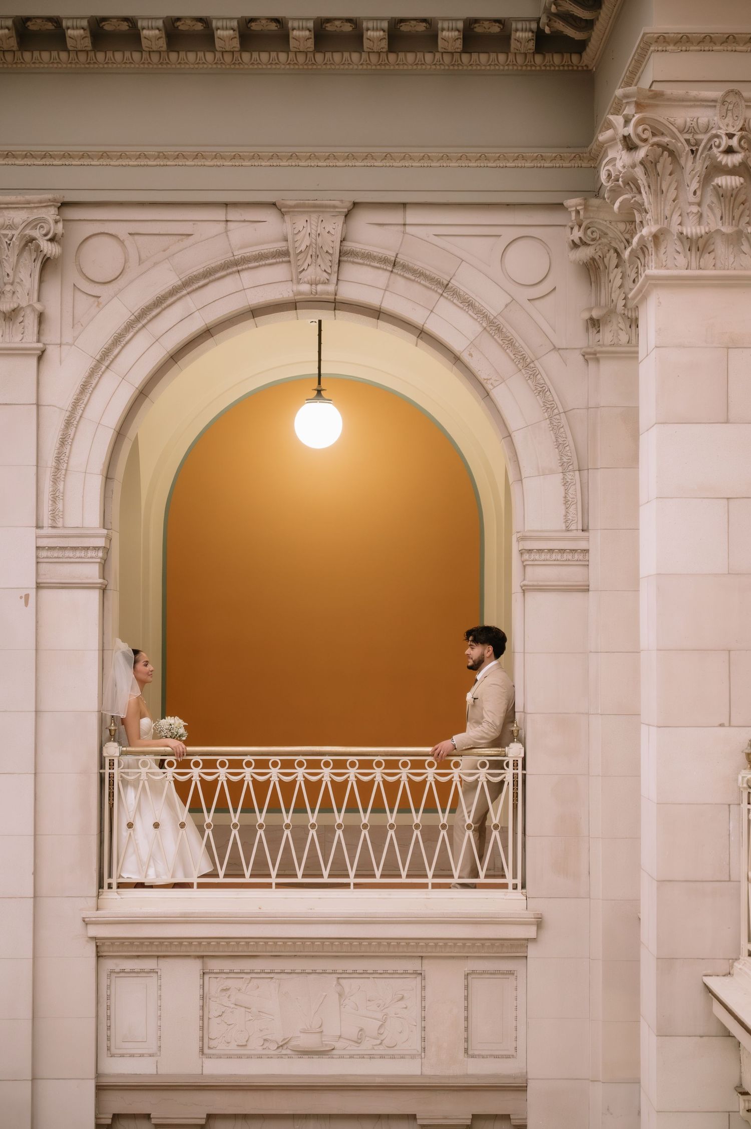 Classic white architectural interior with ornate columns and arches featuring a balcony with decorative railings.