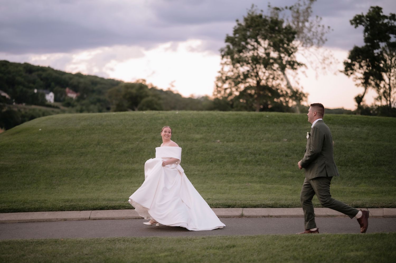 Bride in white gown and groom in suit walking outdoors at sunset on their wedding day.