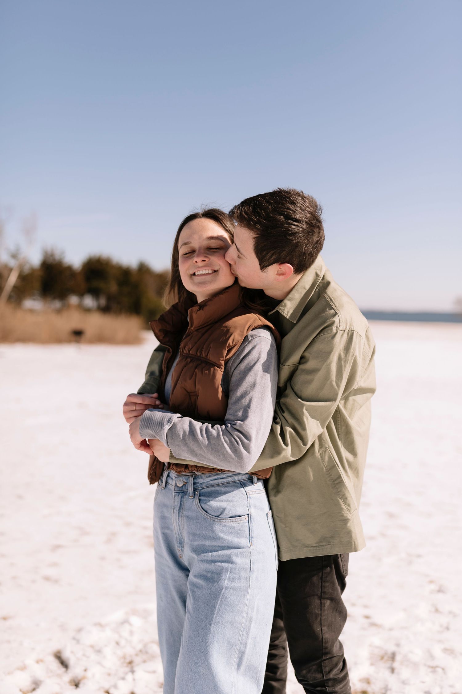 A romantic winter moment shared between a couple embracing on a snowy landscape at sunset.