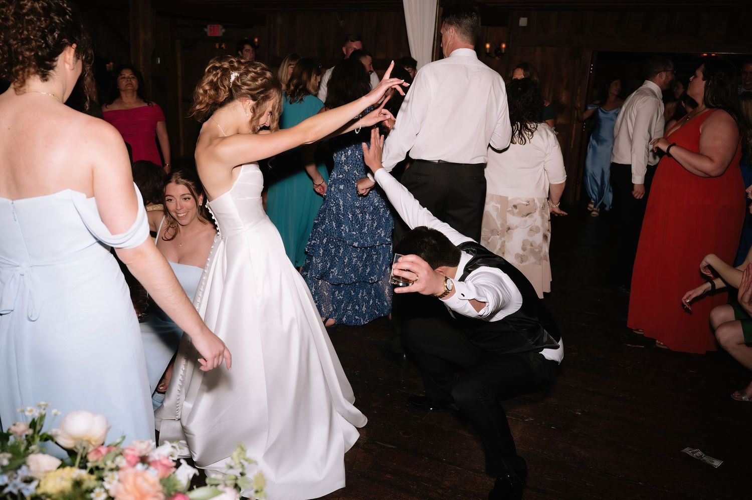 Bride and groom dancing energetically with wedding guests on the reception dance floor.