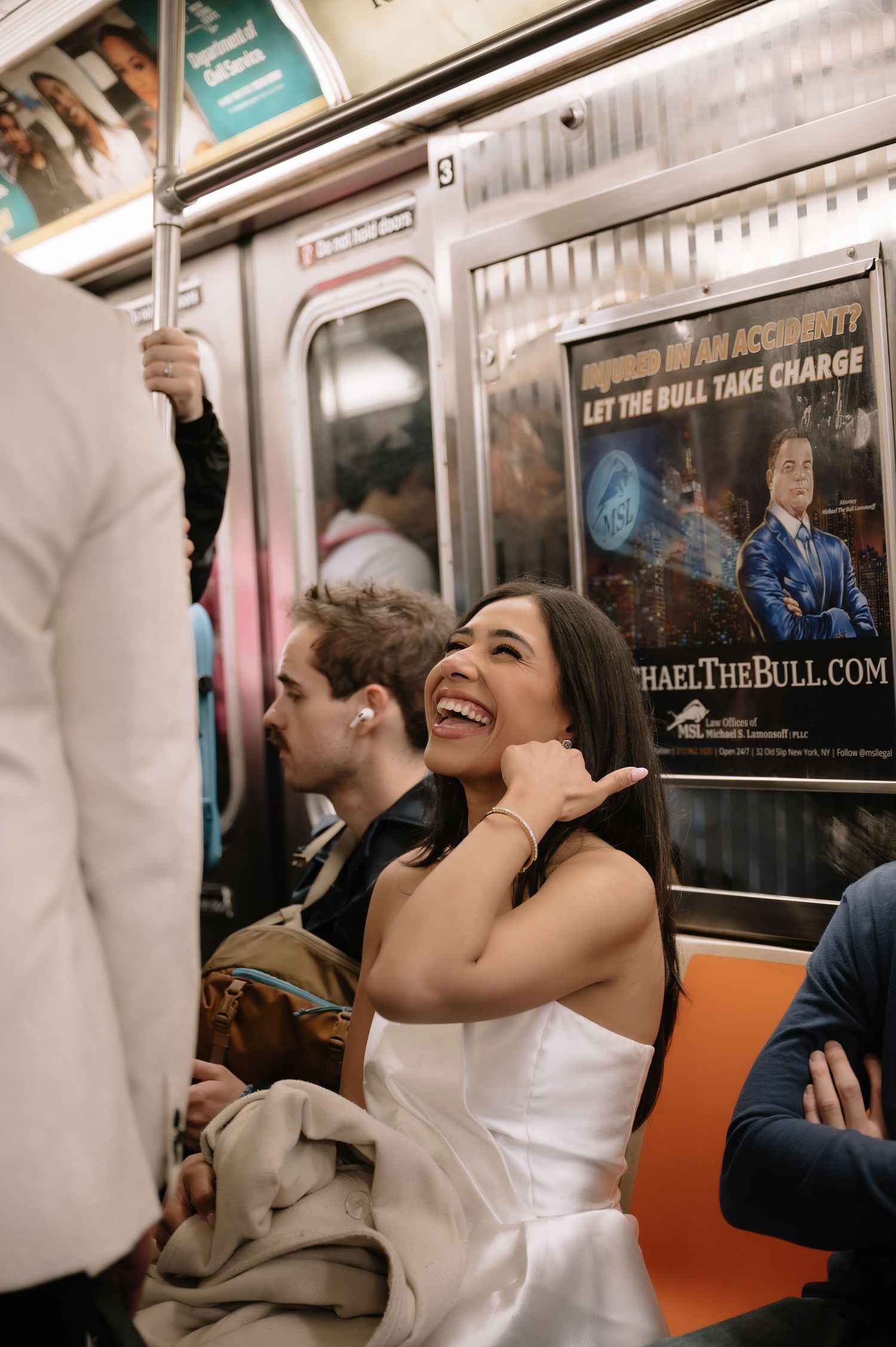 Bride laughing joyfully on subway train while wearing elegant white dress.