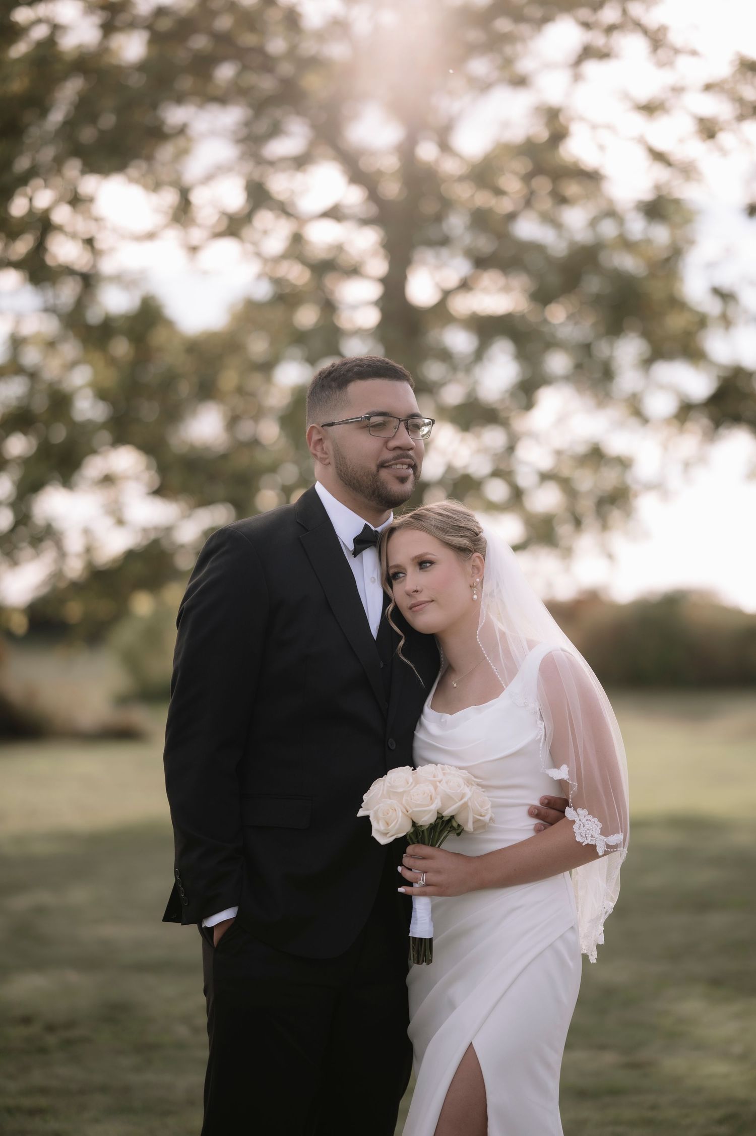 Newlywed couple embraces in an outdoor field during golden hour wedding photoshoot.