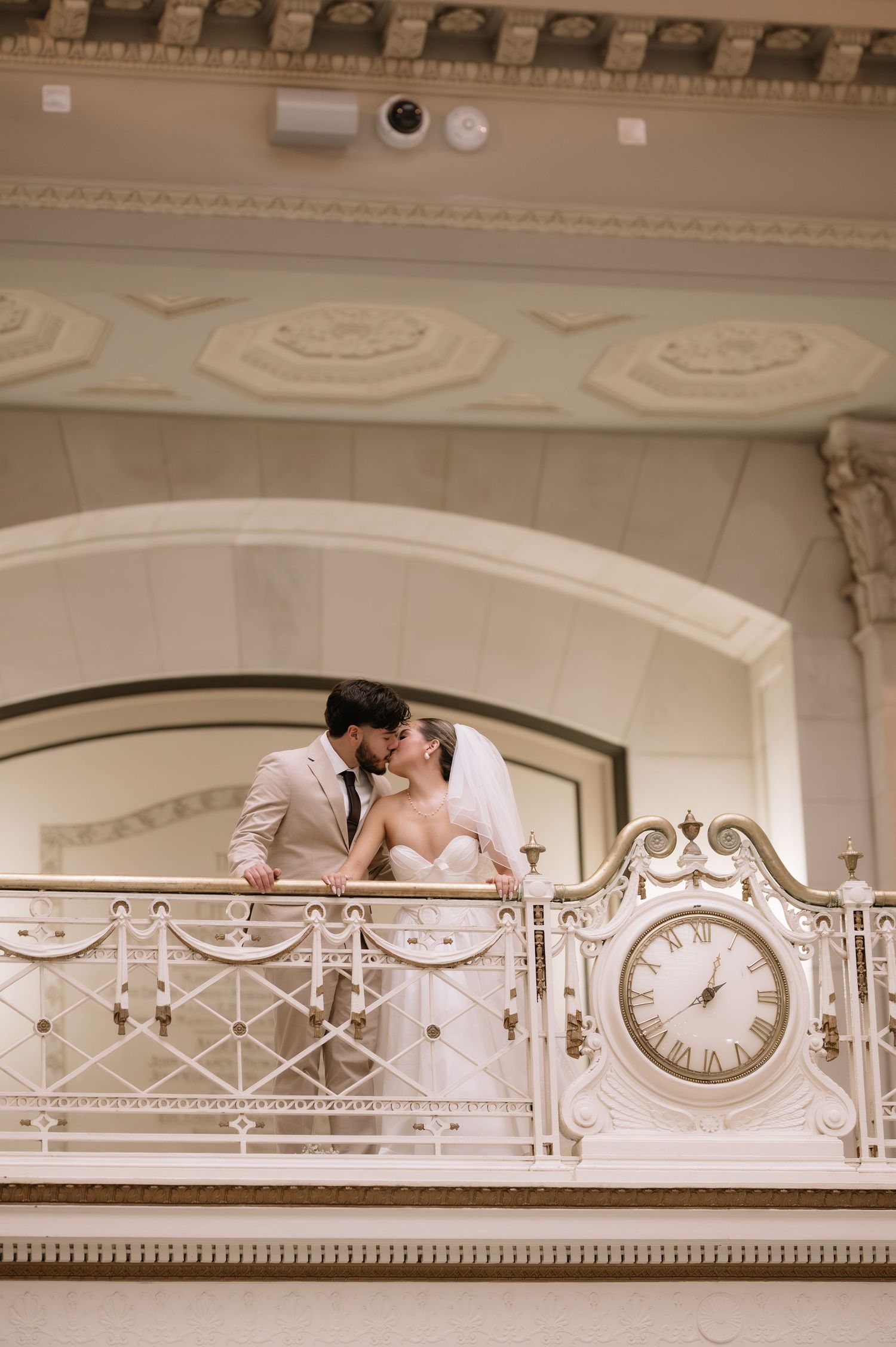 Romantic moment captured on an ornate white balcony with decorative moldings and a vintage clock.
