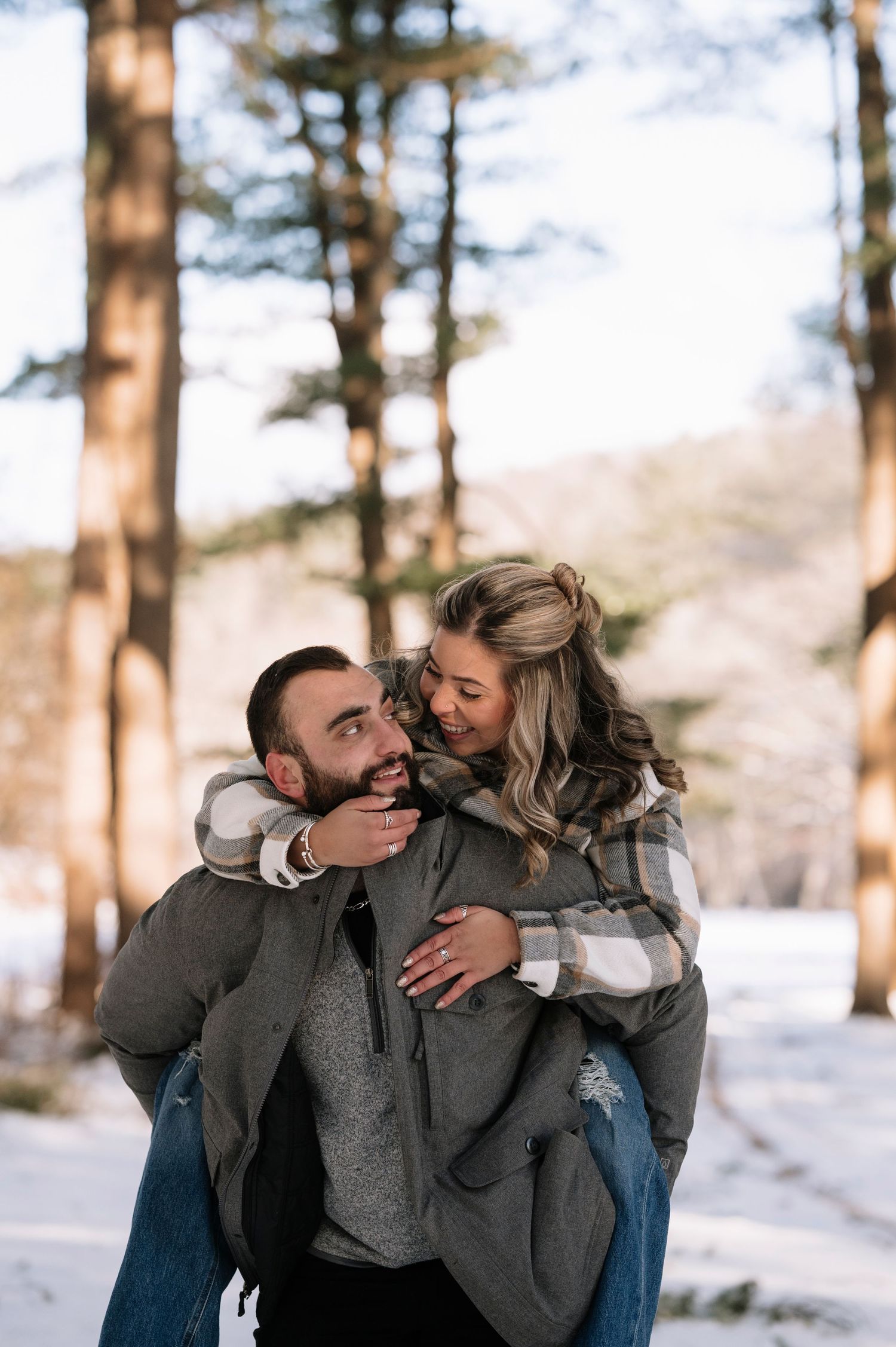 A playful piggyback ride moment between a couple in a snowy forest setting.