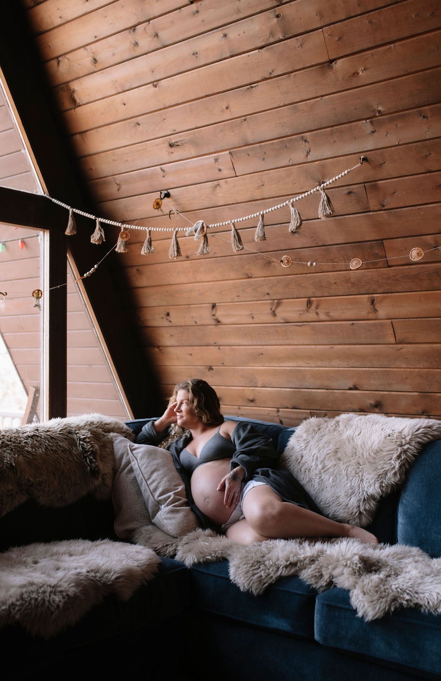 A cozy cabin interior with a blue couch adorned with fluffy sheepskin throws and string lights on wooden walls.
