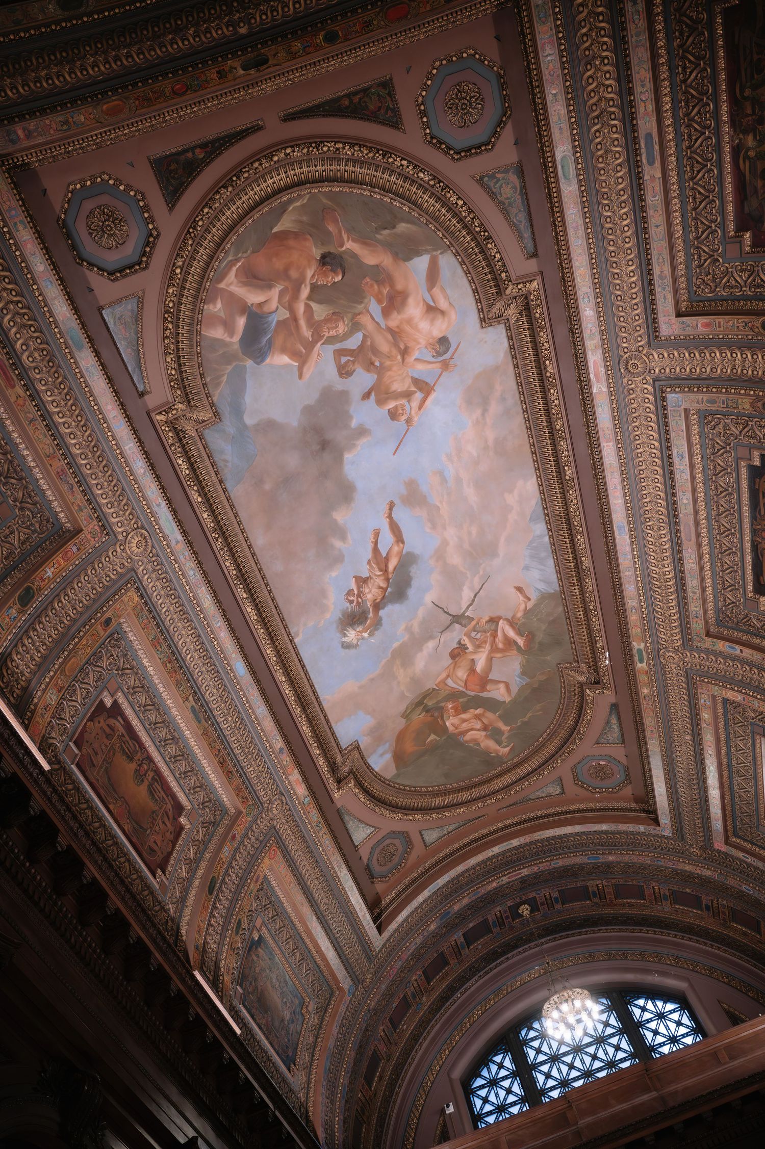 Ornate baroque ceiling fresco with painted cherubs and celestial figures floating among clouds in an architectural frame.