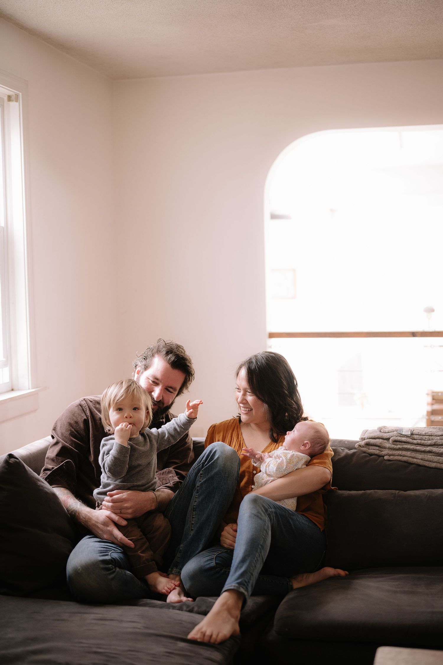 Family sharing laughs and cuddles on a dark gray couch in a bright, modern living room.