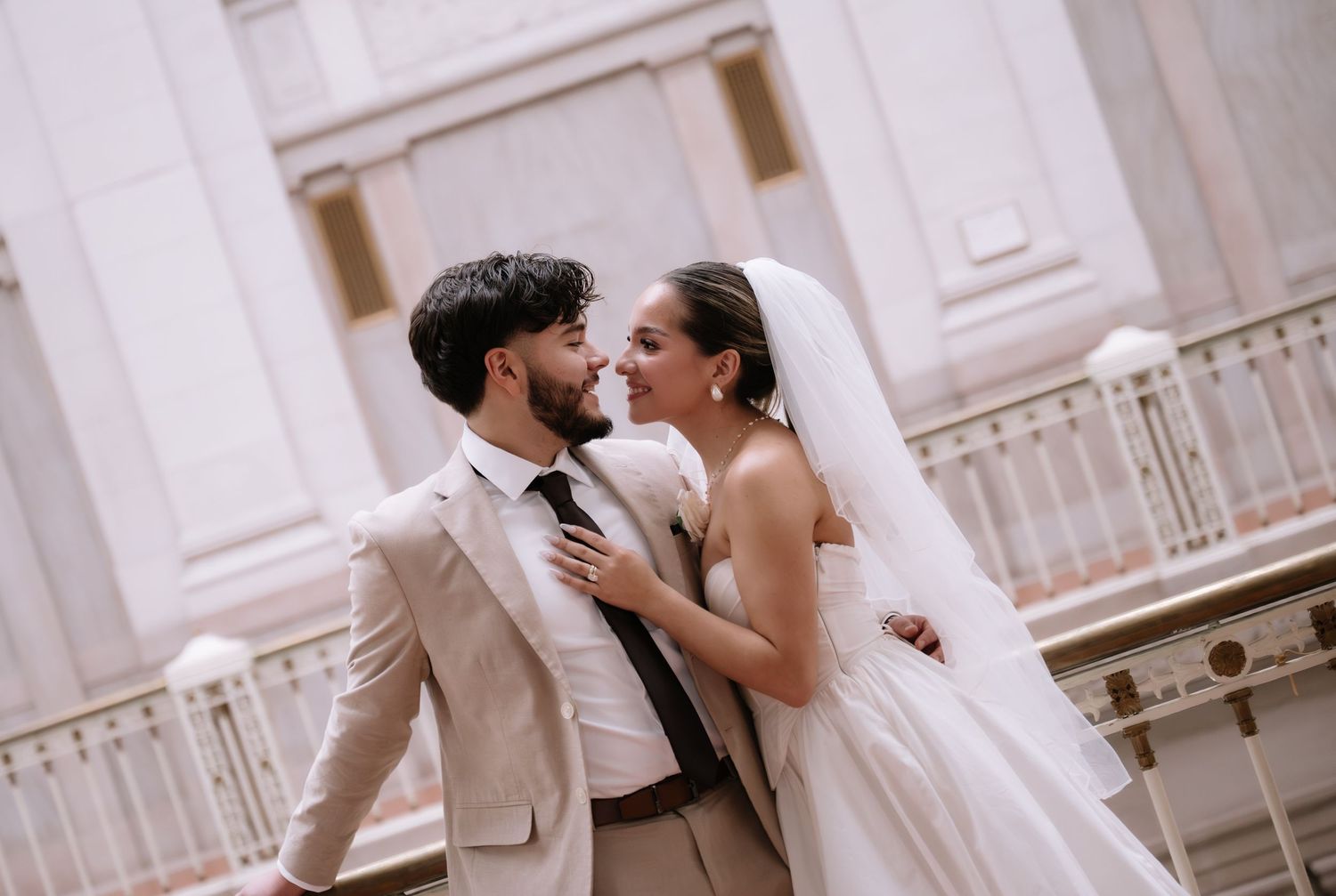 A bride and groom share an intimate moment in front of an elegant white stone building.