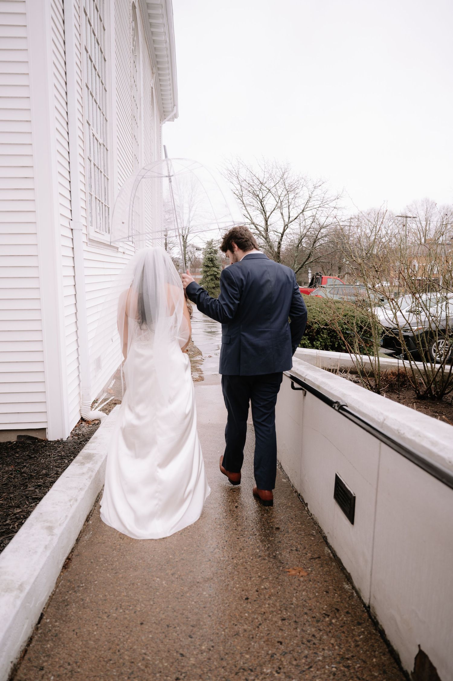 Wedding couple walking along snowy church pathway in winter.