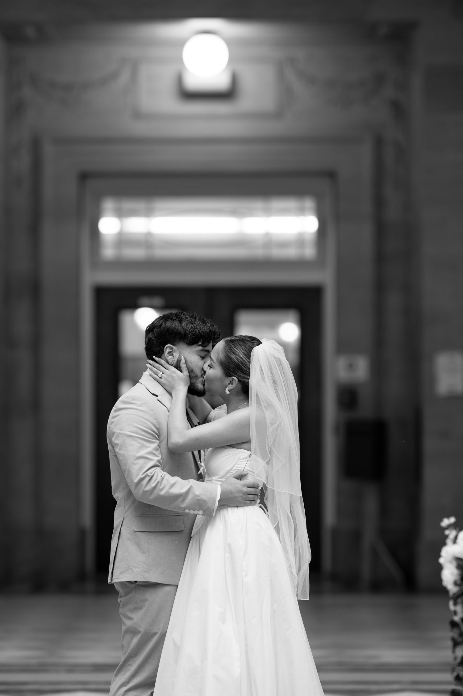 A romantic black and white photo of newlyweds sharing an intimate moment in an elegant hallway.