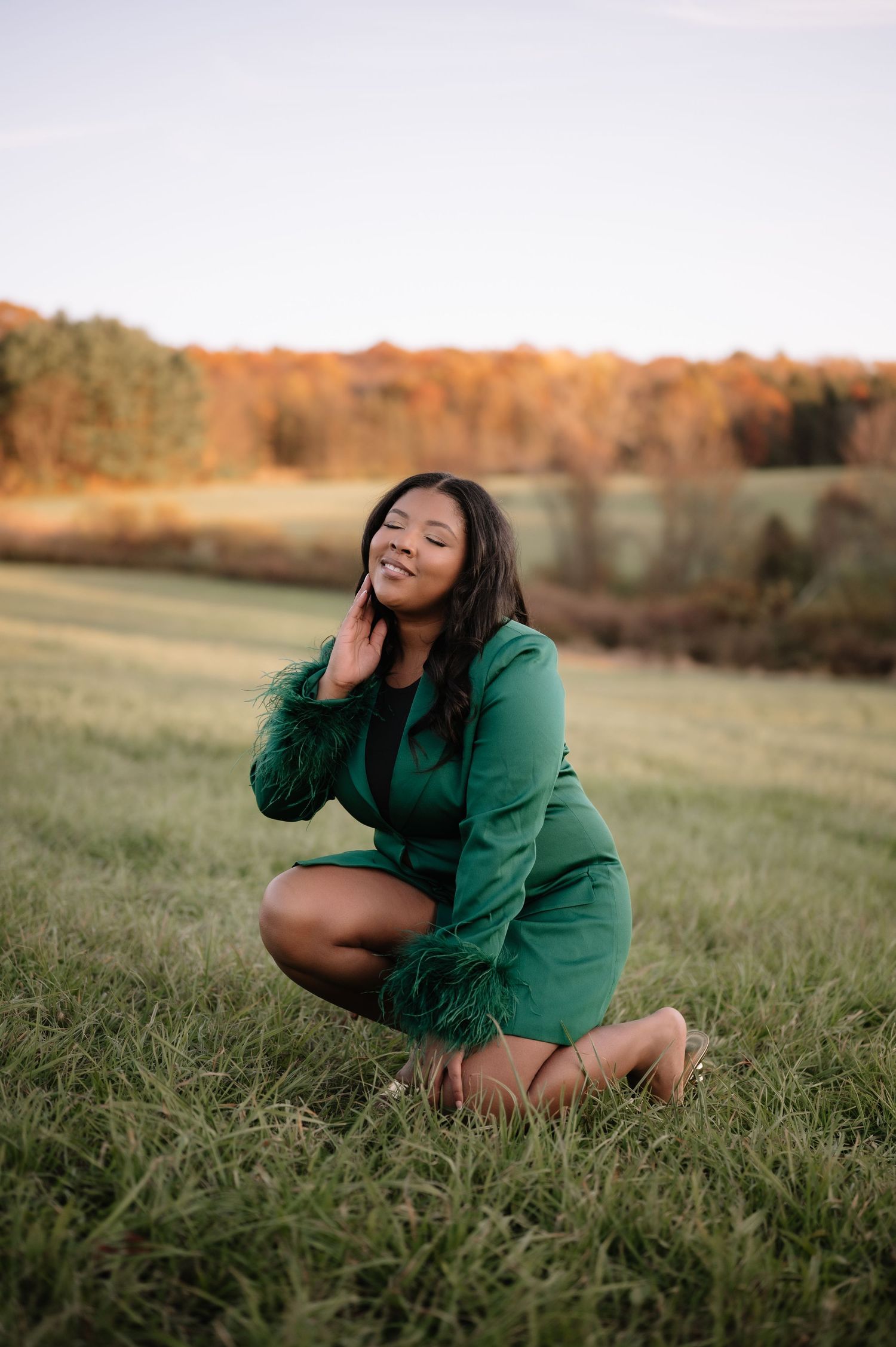A person in a green blazer poses expressively while sitting in a grassy field during golden hour.