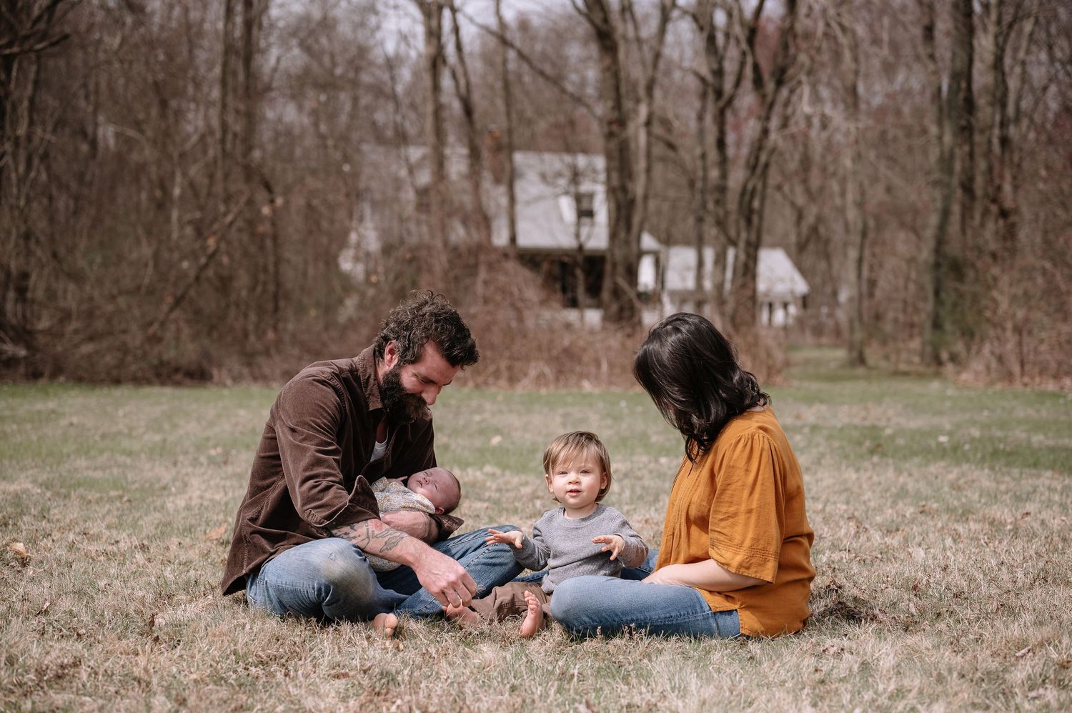A family sits together on grass having a tender moment outdoors.