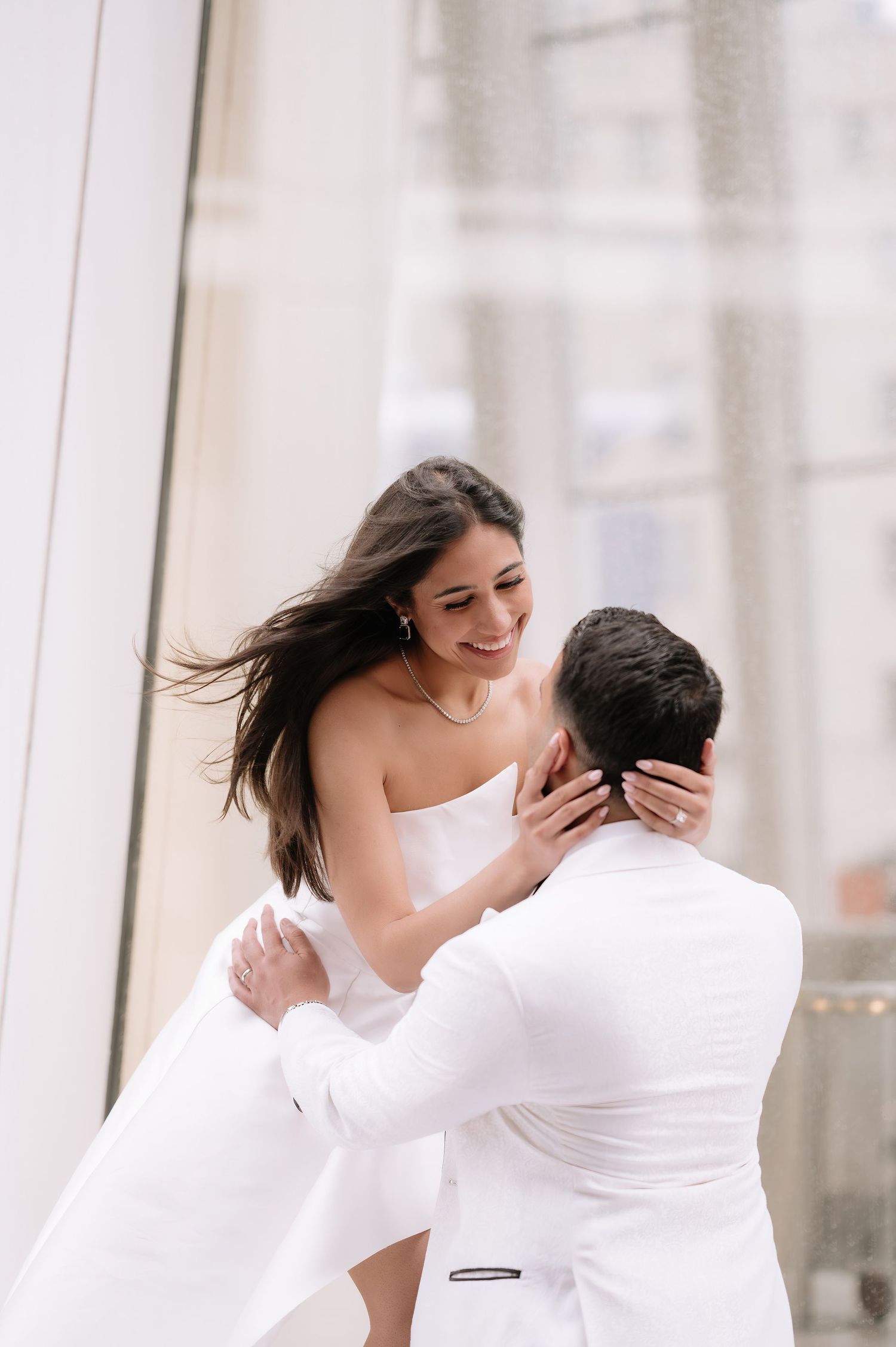 Candid moment of couple in white formal wear sharing an intimate embrace.