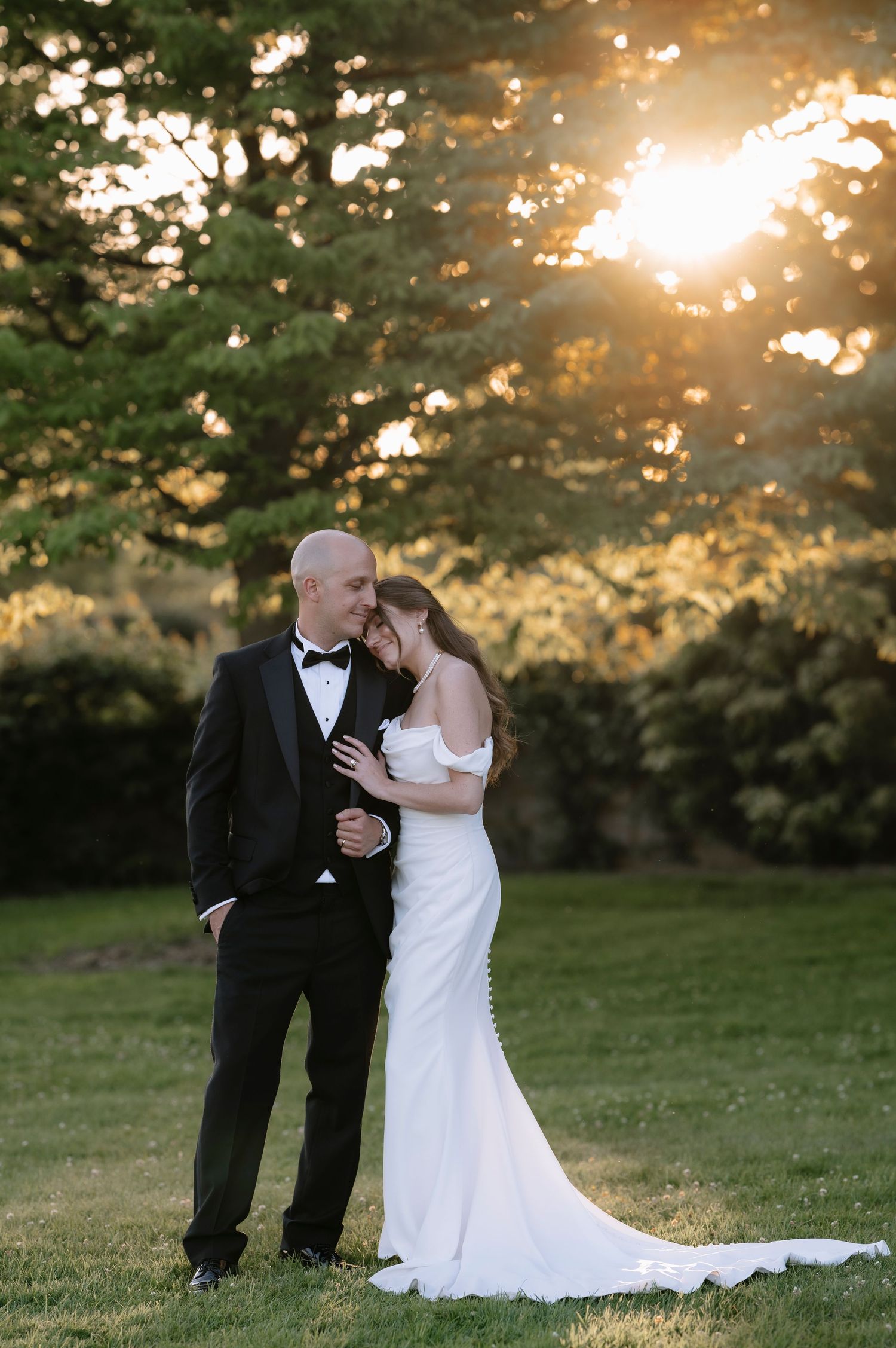 A couple shares an intimate moment during their wedding ceremony at sunset in a grassy field.