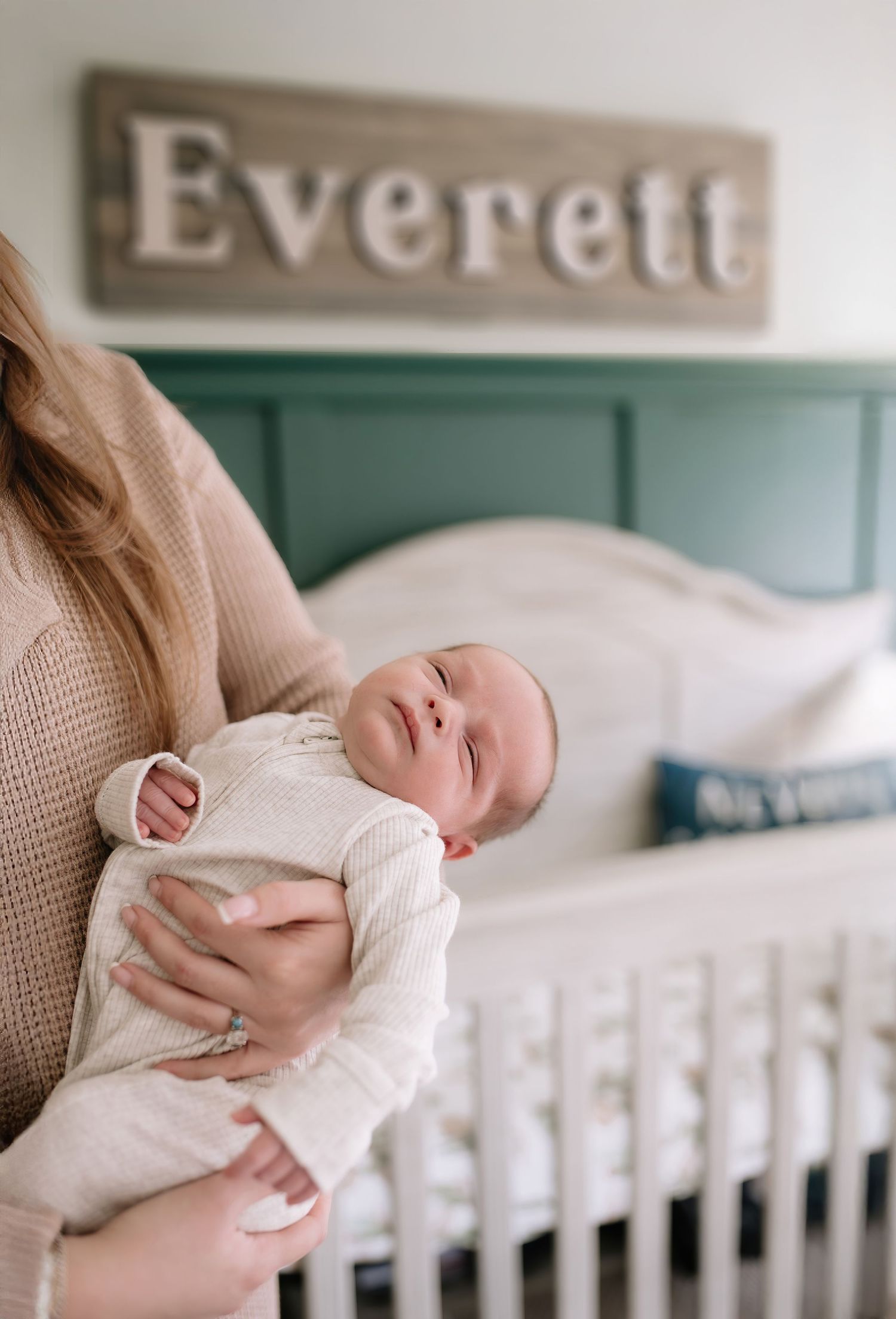 A sleeping newborn baby in white clothing beneath a wooden 'Everett' name sign in a nursery.