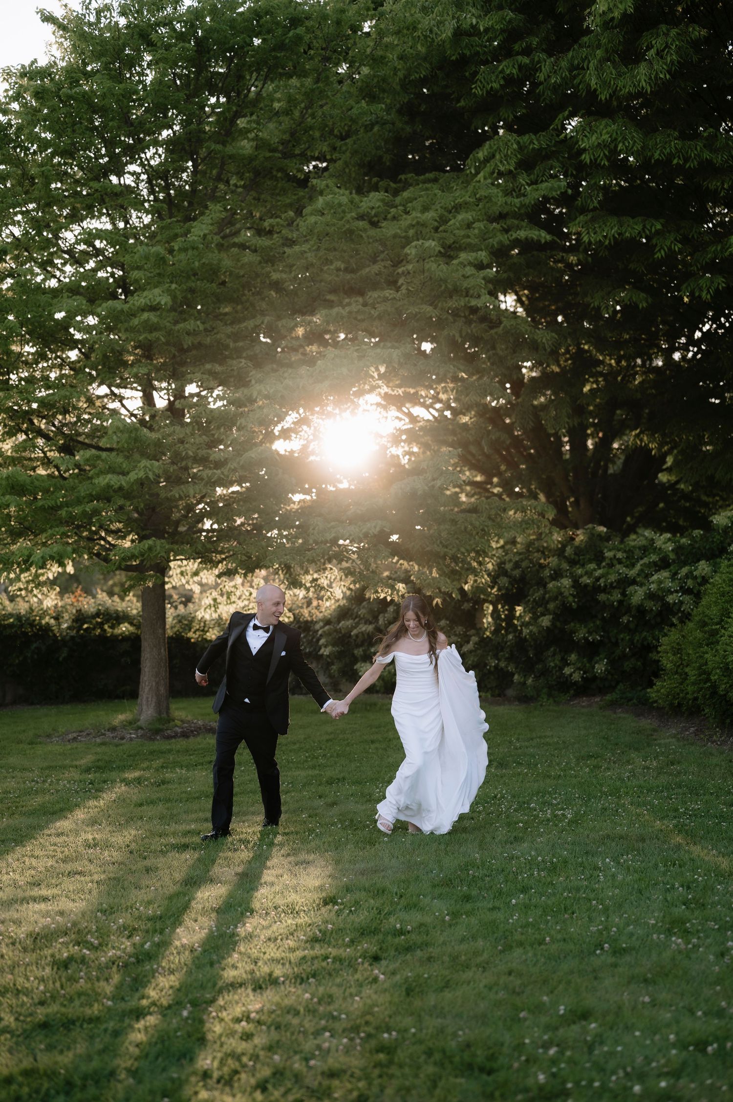 A romantic sunset wedding photo shows a couple holding hands on a grassy lawn framed by trees casting long shadows.