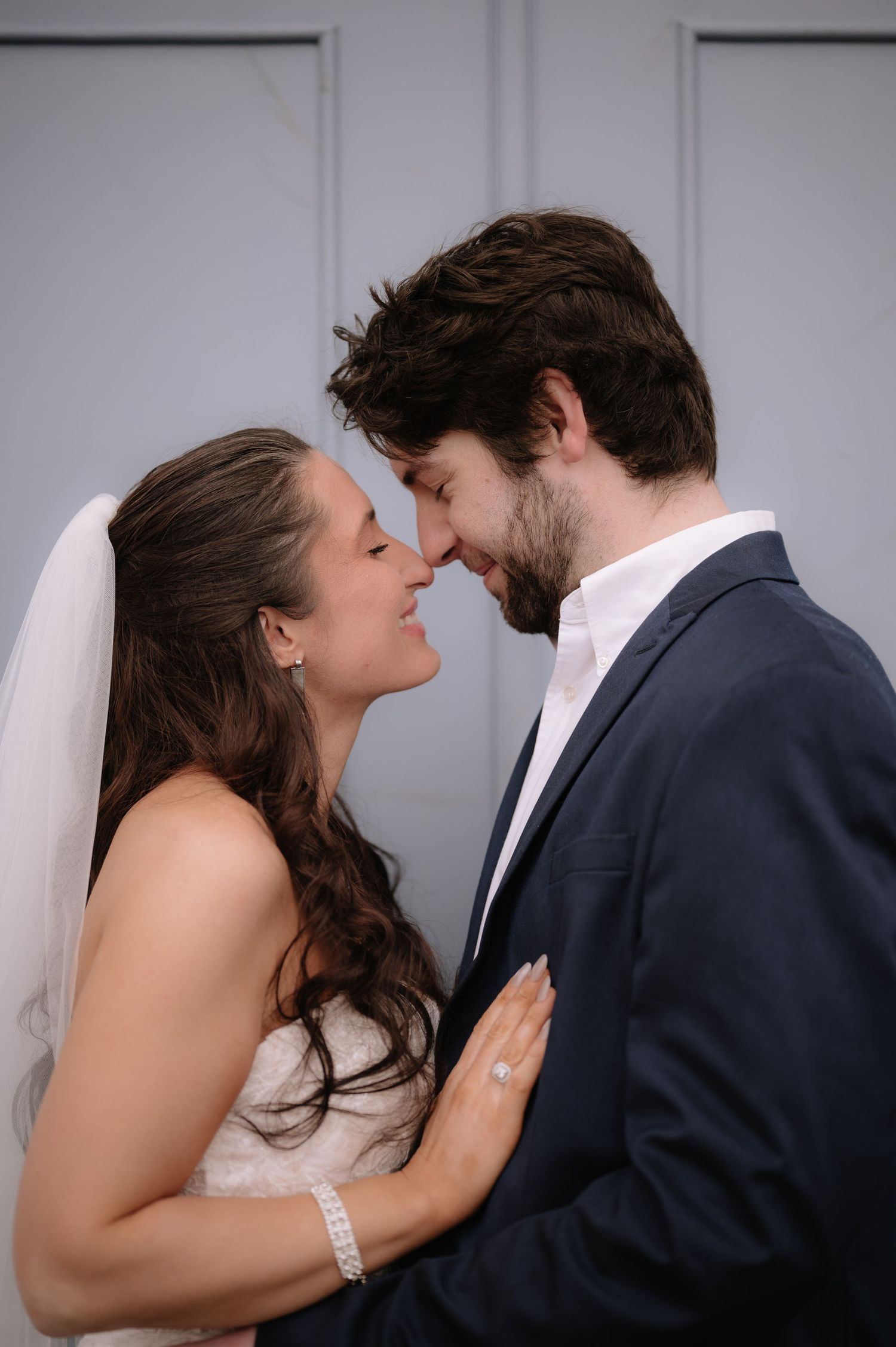Tender moment captured in wedding portrait against light gray wall.