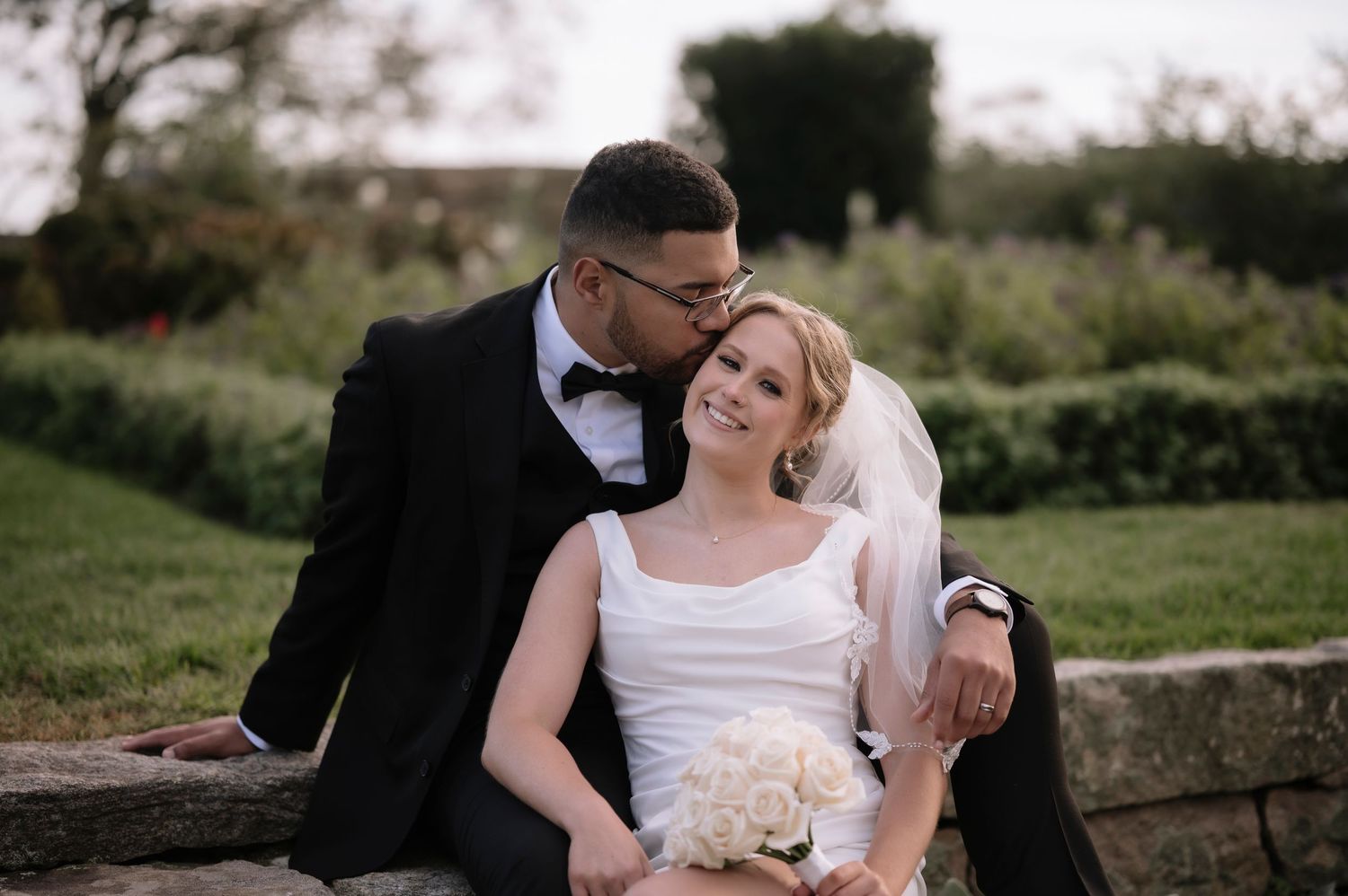 A romantic outdoor wedding photo of a couple sharing an intimate moment in a garden setting.