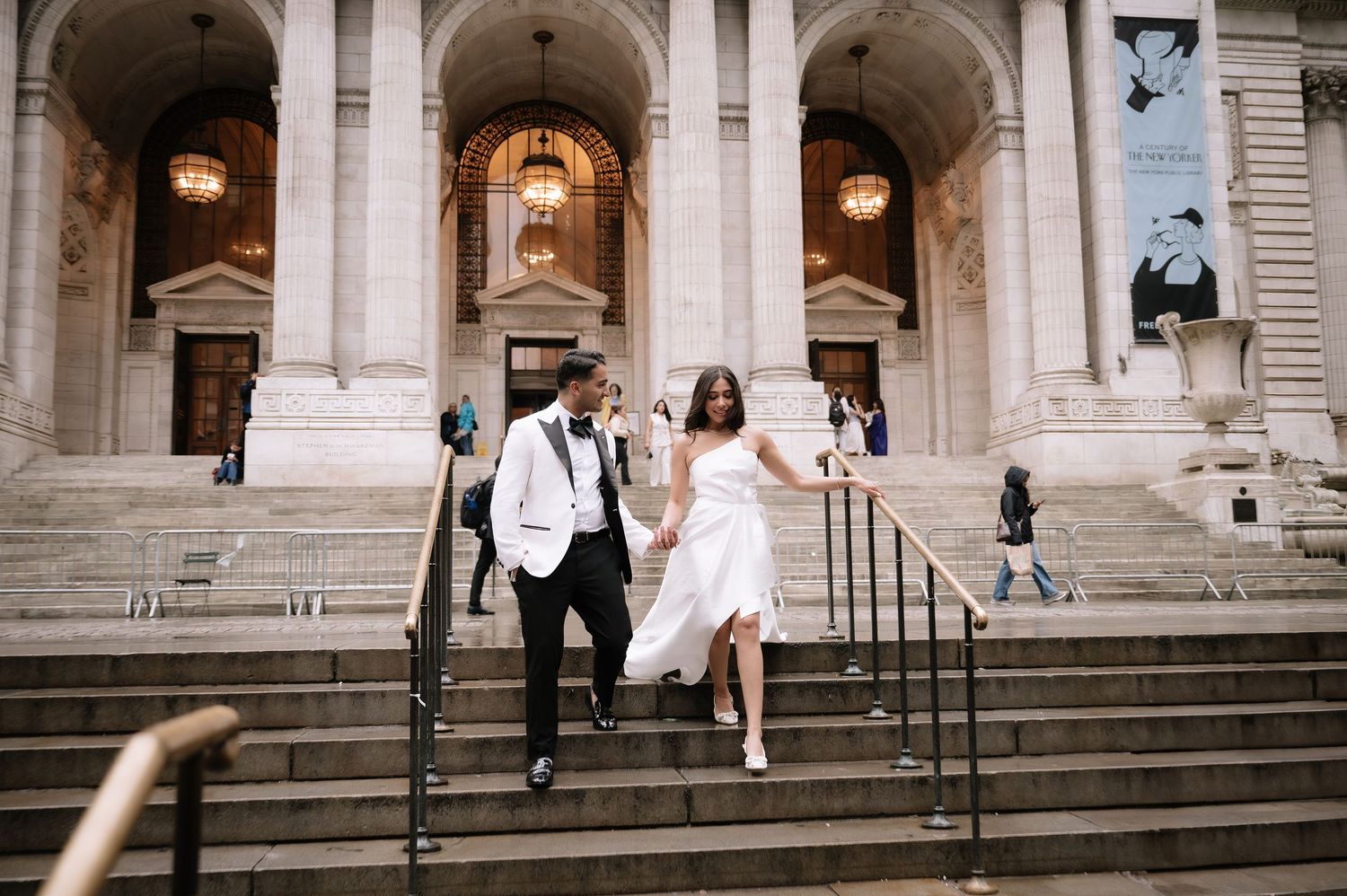 A couple in elegant wedding attire joyfully descends the grand steps of New York Public Library.