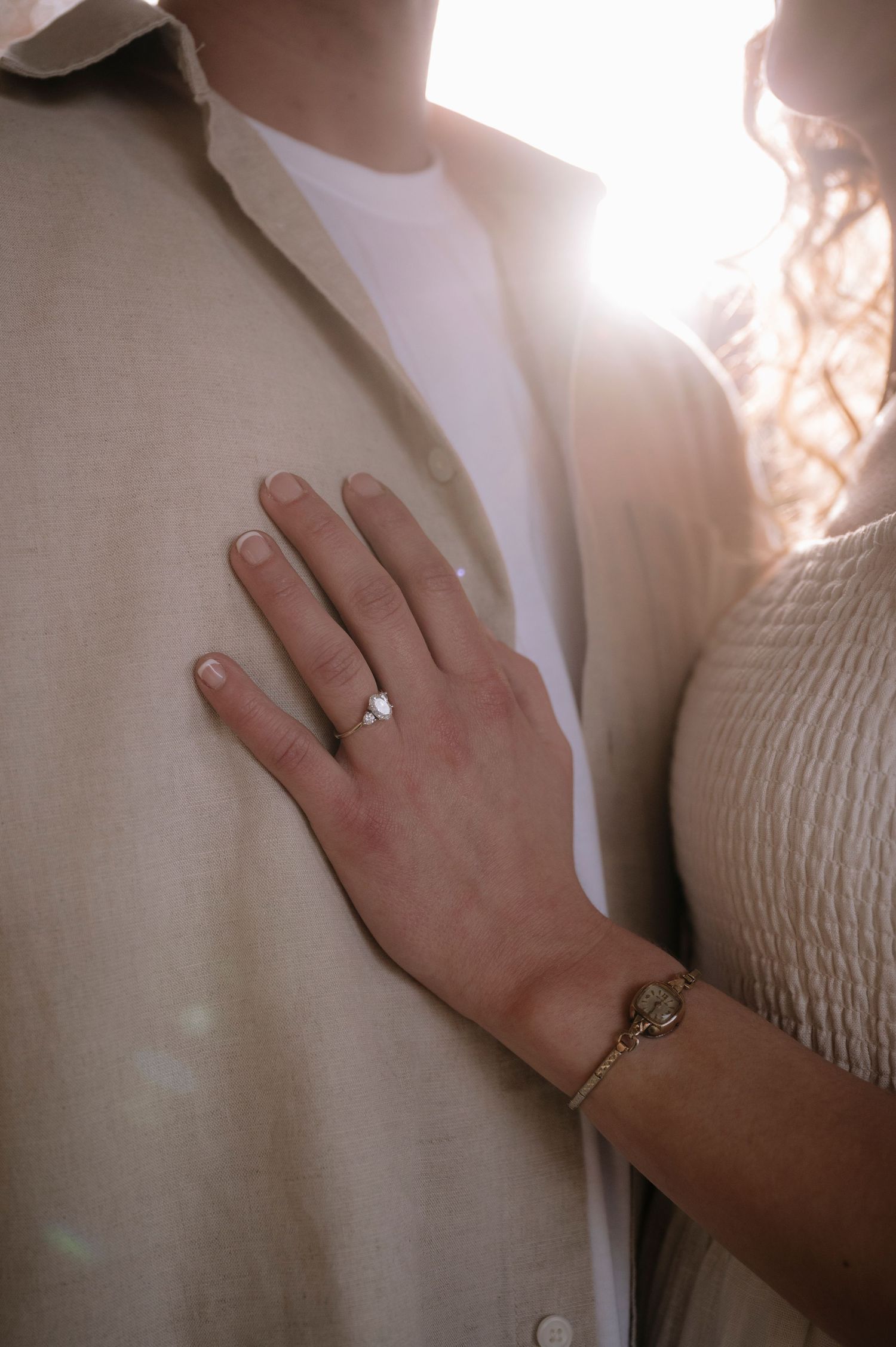 Close up of engagement ring and bracelet on hand against beige clothing.