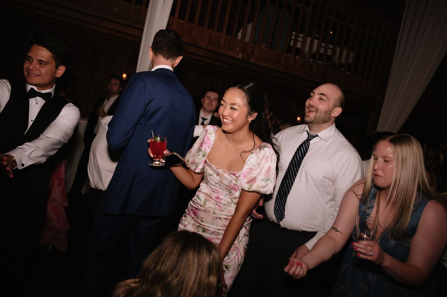 Happy wedding guests laughing and socializing on the dance floor during a festive reception celebration.