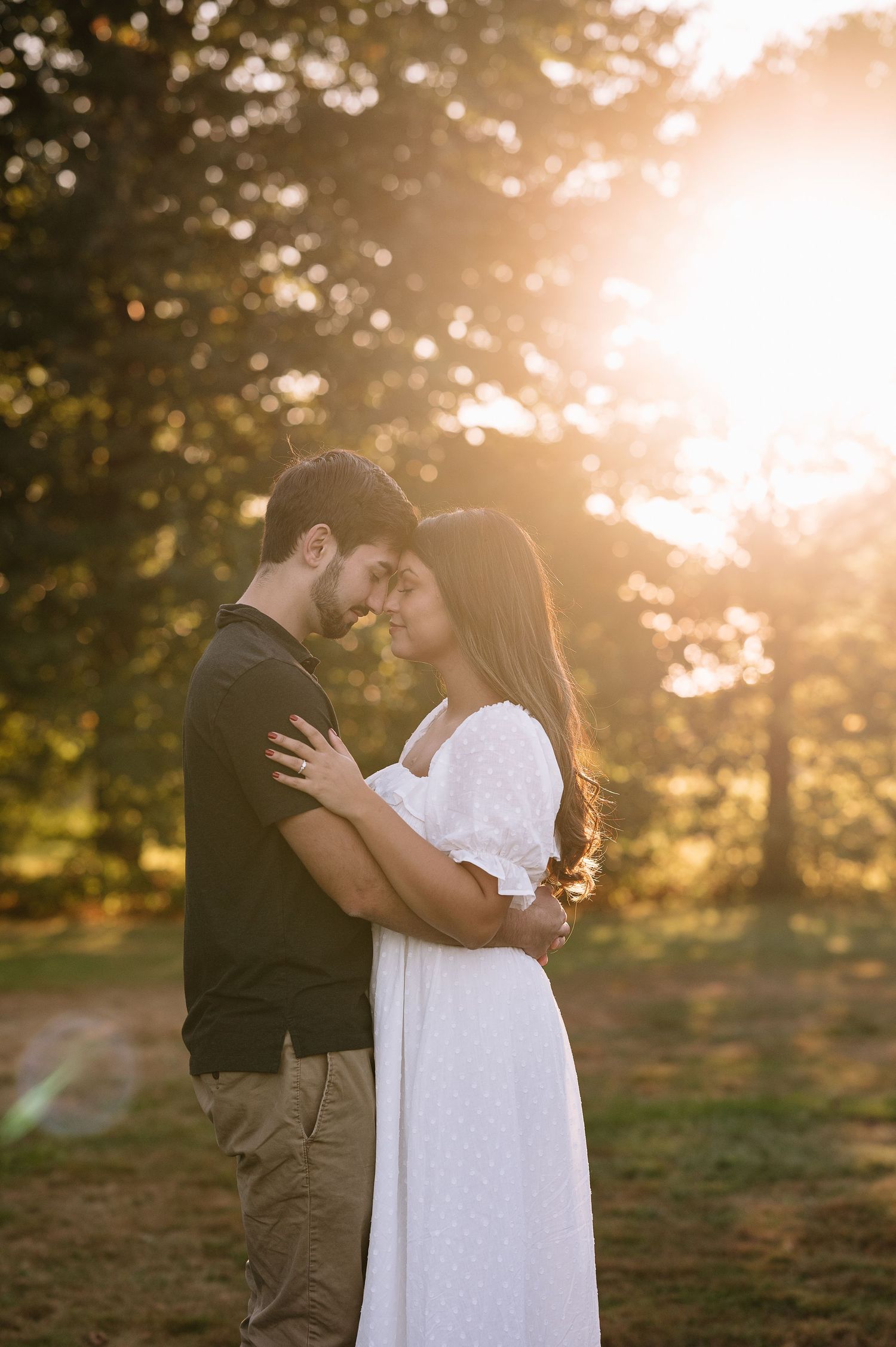 An intimate embrace during golden hour with sunlight filtering through trees in the background.