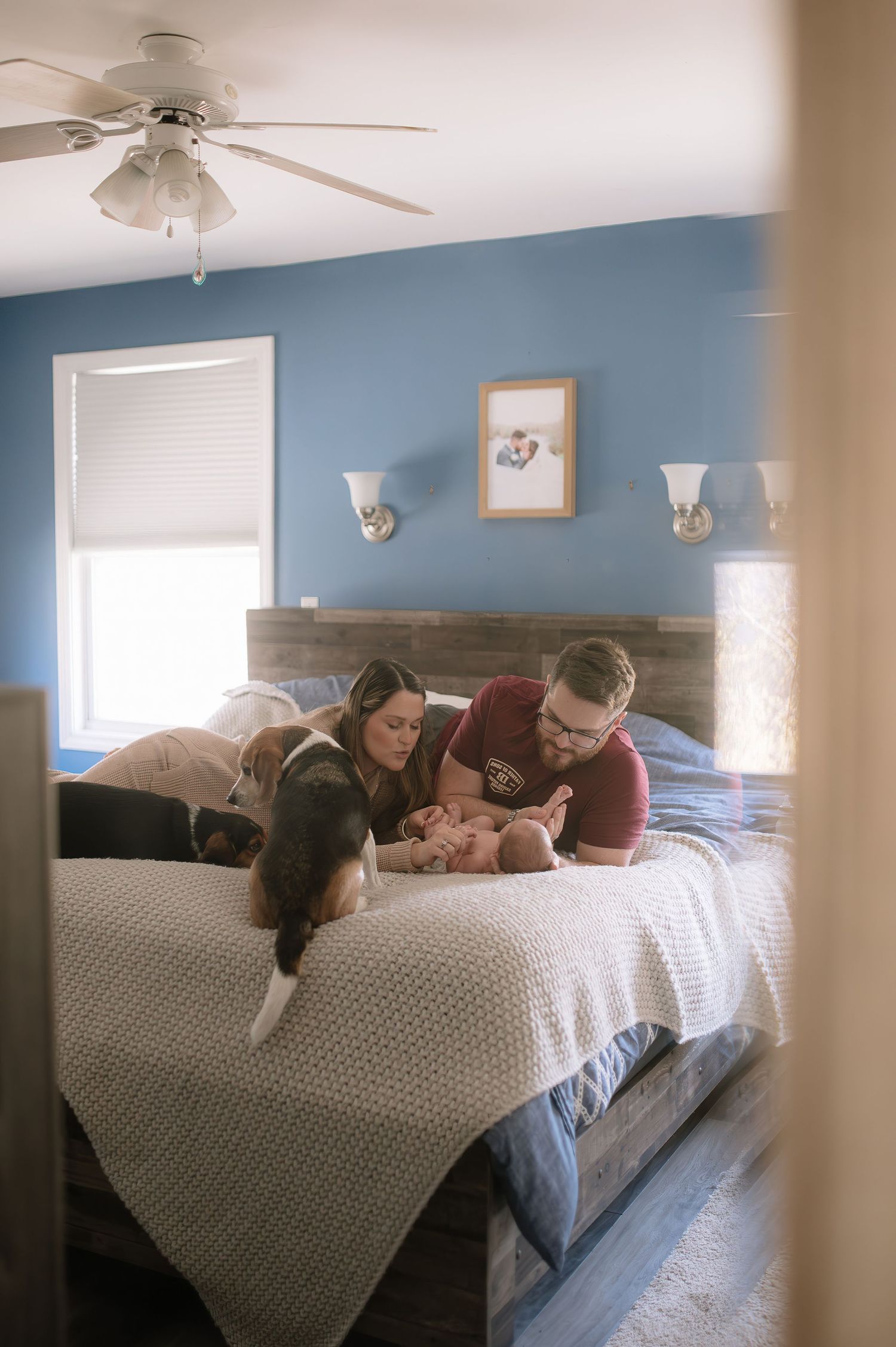 A couple and their dog share a quiet moment on their bed in a blue-walled room.