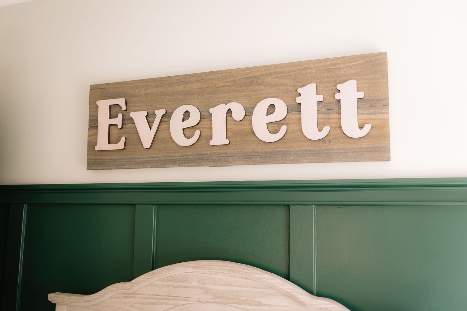 A wooden sign with the name 'Everett' mounted on a wall above green paneling.