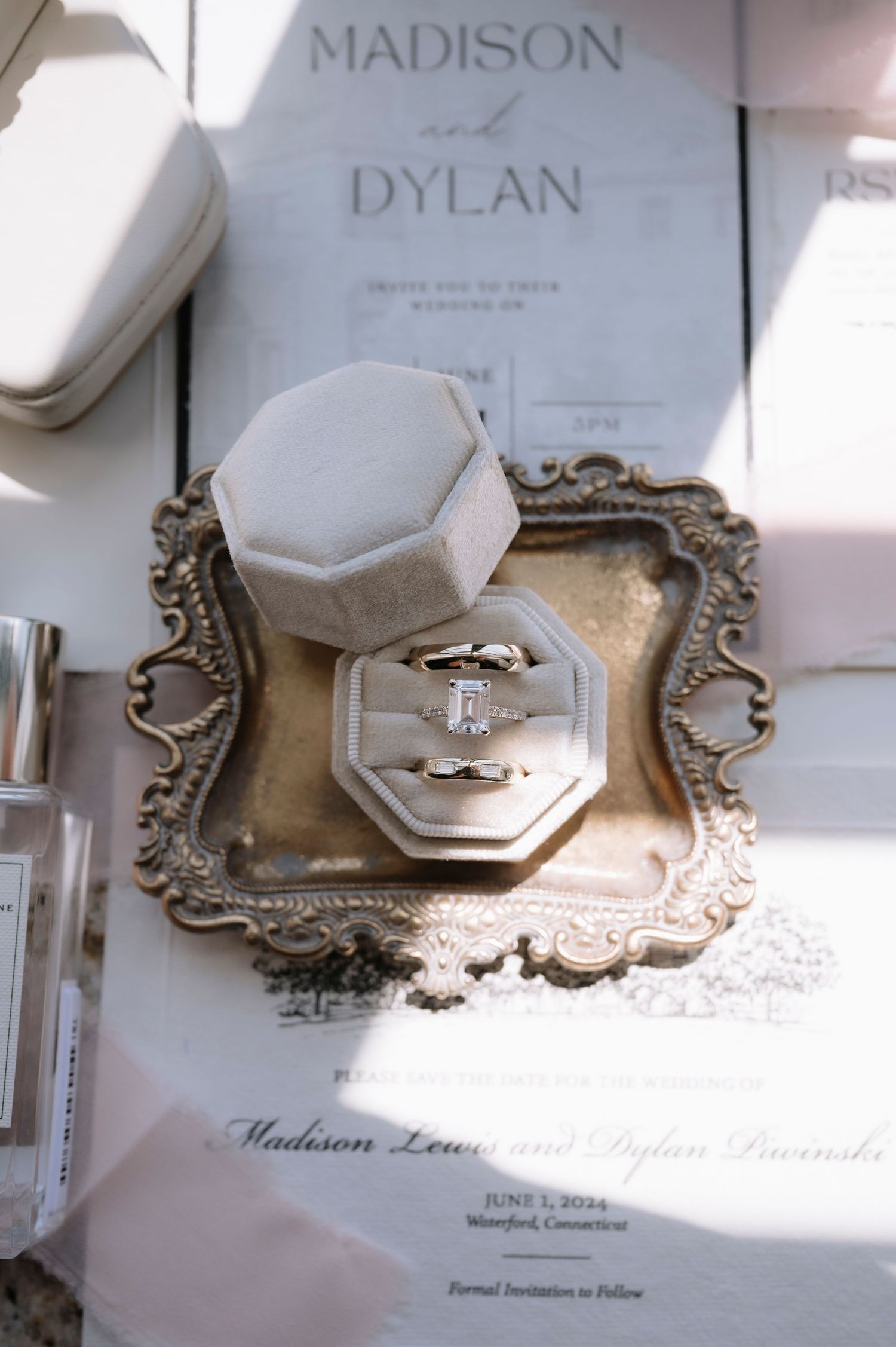 Wedding rings displayed in a hexagonal white box on an ornate silver tray beside a Madison and Dylan invitation.