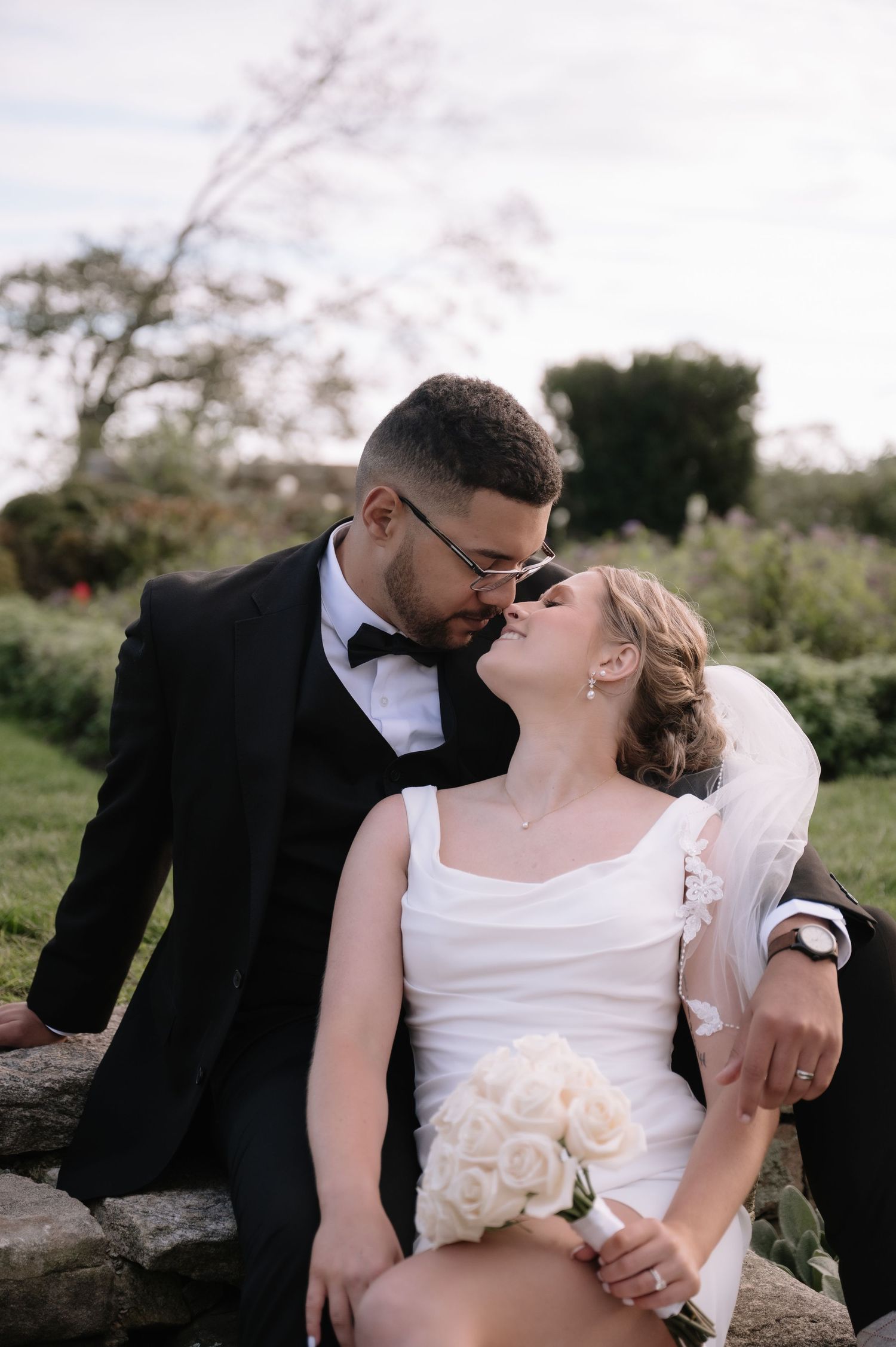 Newlyweds share intimate moments on rustic stone wall surrounded by natural outdoor scenery.