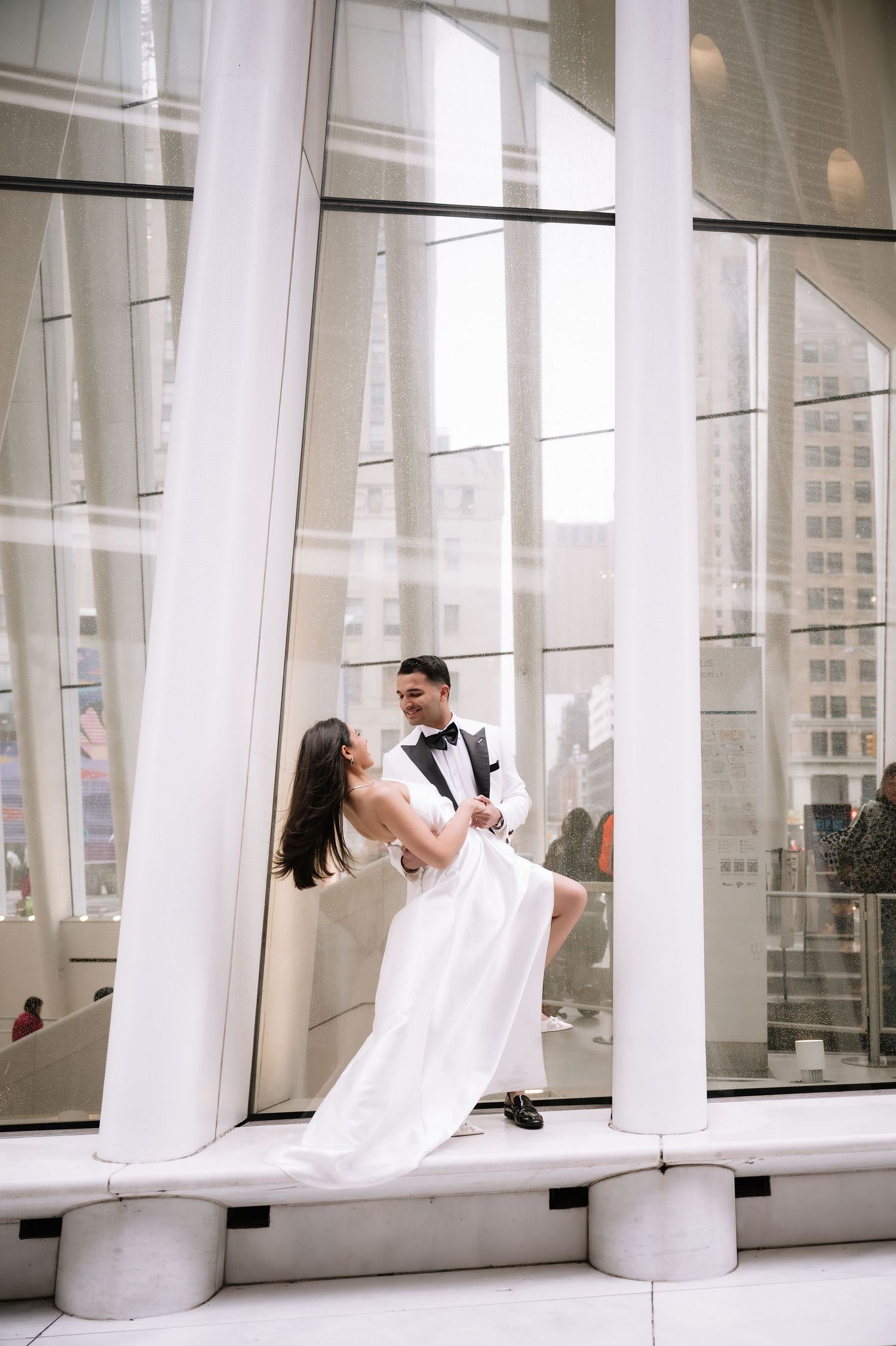 Dancing couple in formal wear posing dramatically between tall white architectural columns.